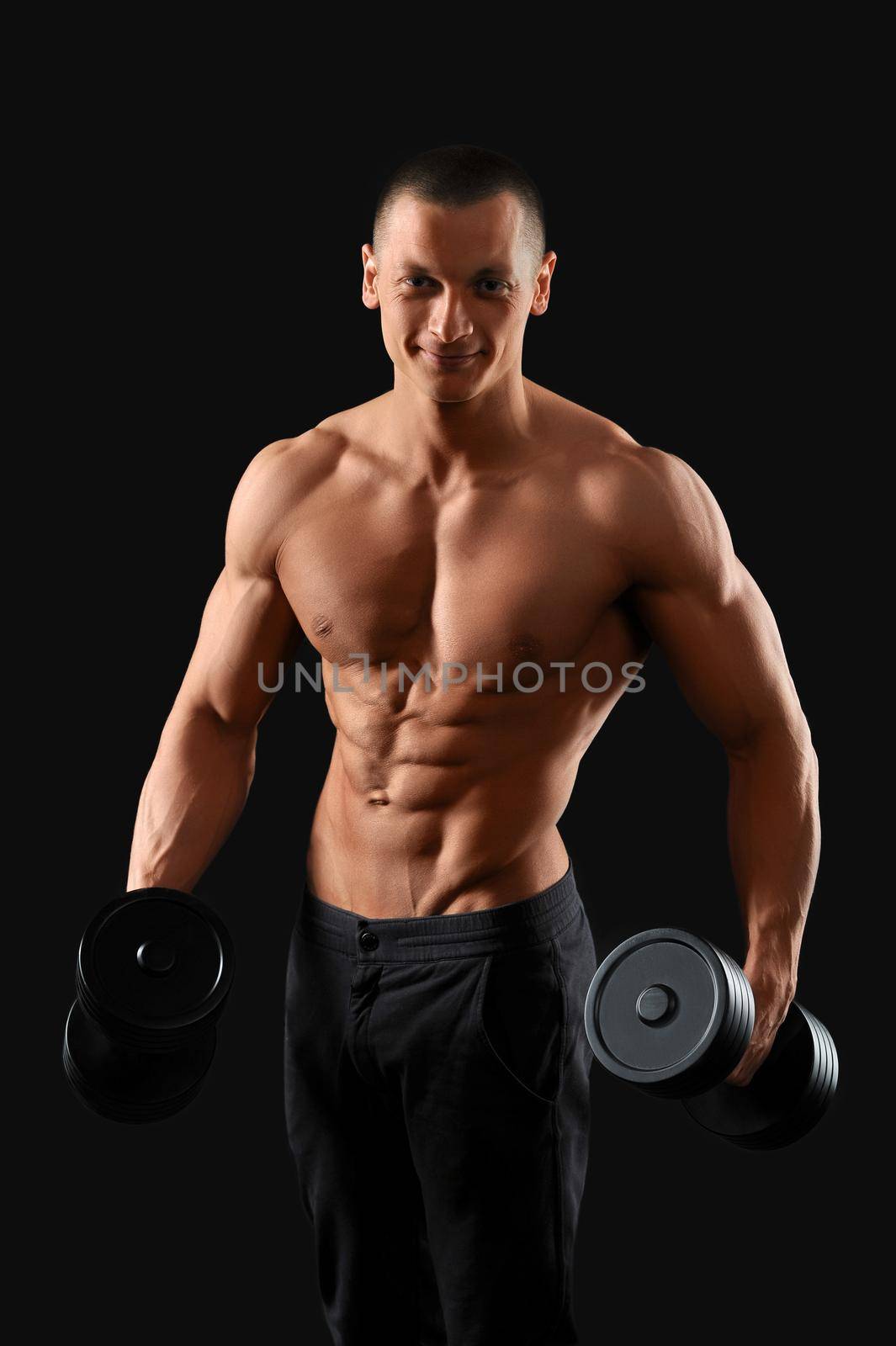 Tuned body. Studio portrait of a young handsome fitness man posing with a dumbbell showing off his stunning muscled torso on dark background