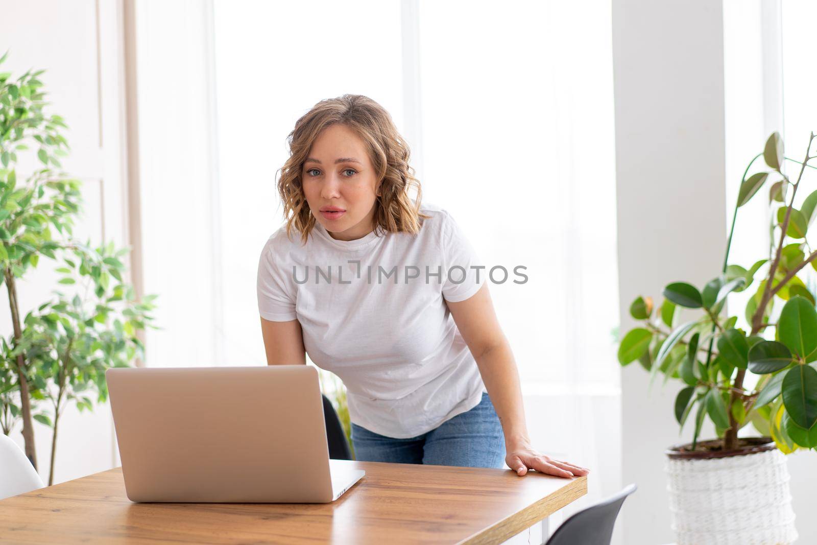 Business woman using laptop standing near desk white office interior with houseplant looking at camera Business people Business person Online, Young and successful Dresed white shirt and jeans