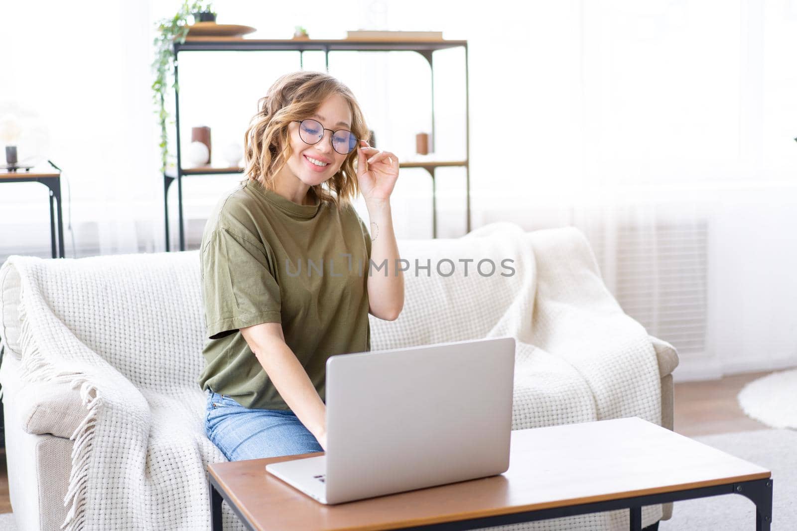 Woman with glasses use laptop typing keyboard sitting couch big window background home interior Freelance female working from home Distance learning student relaxing watch lessons video conference.