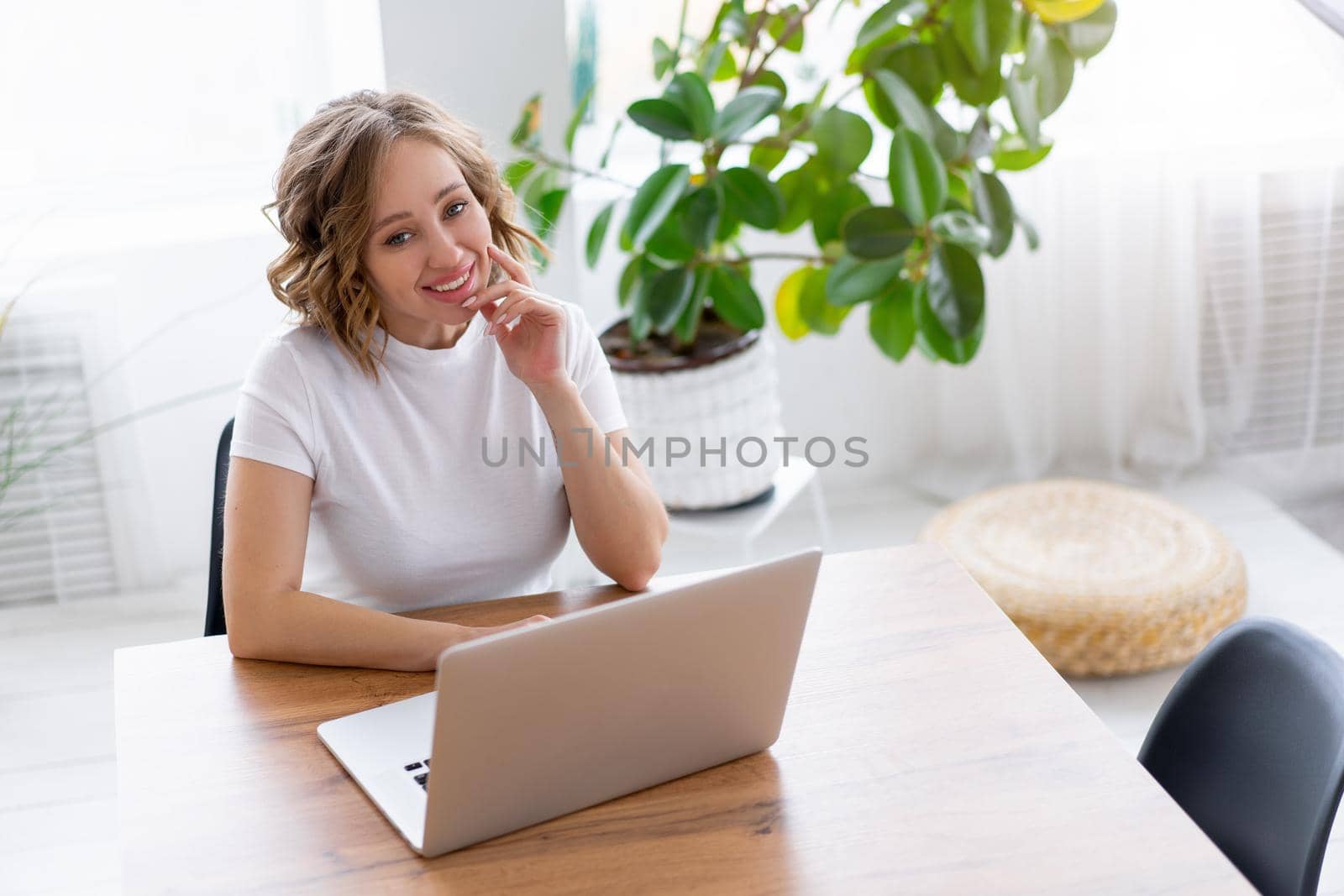 Business woman using laptop sitting near desk white office interior with houseplant looking at camera by andreonegin