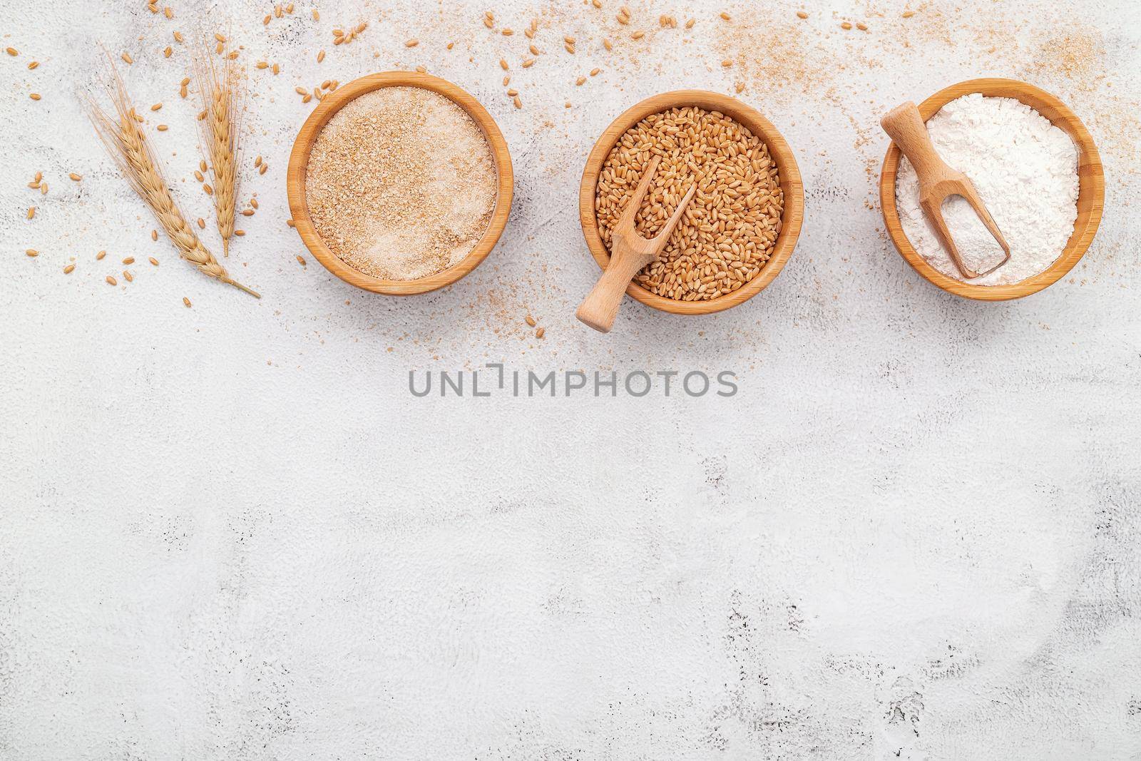 Wheat grains , brown wheat flour and white wheat flour in wooden bowl set up on white concrete background.