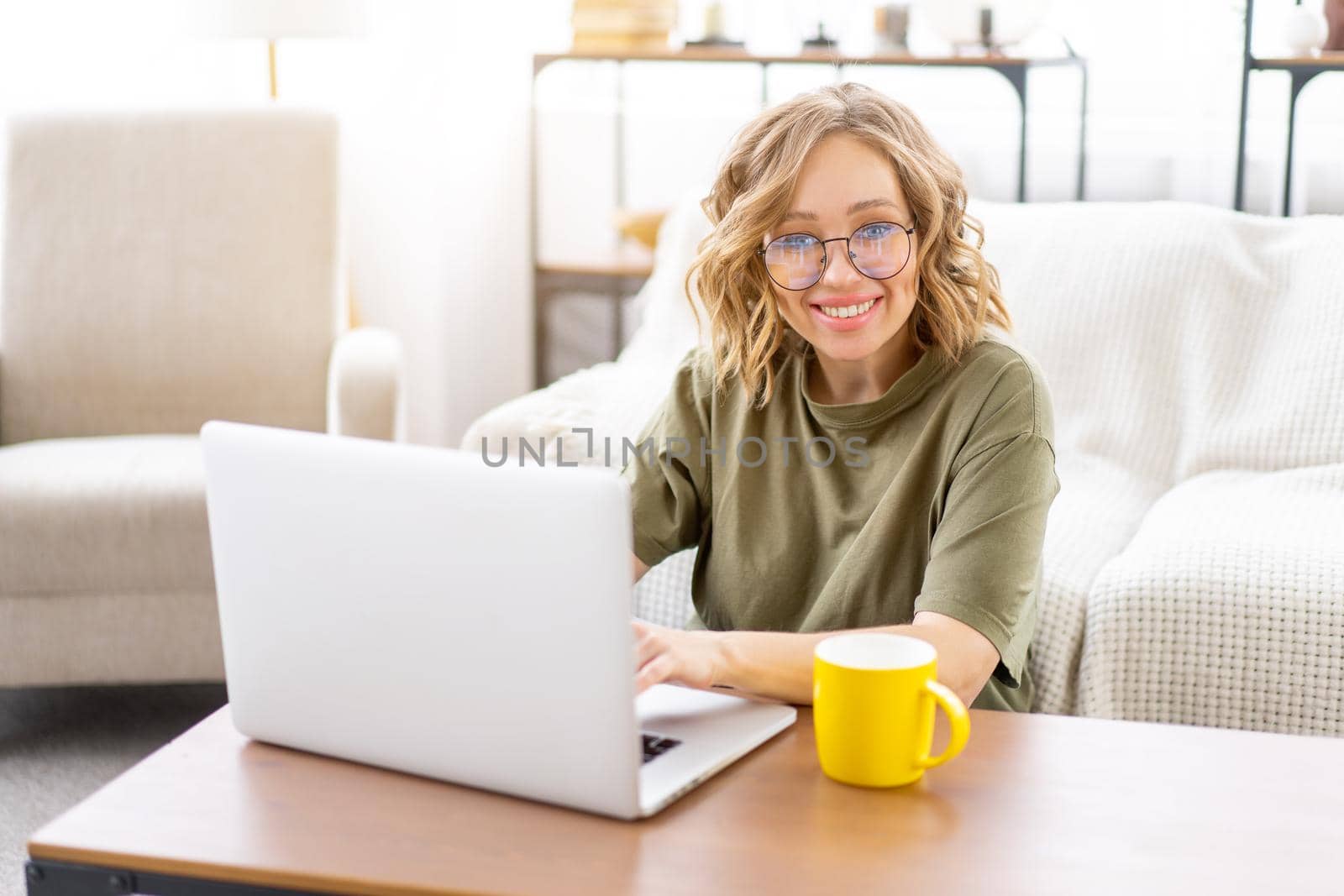 Woman glasses using laptop computer while sitting near sofa with big window on background at home interior by andreonegin