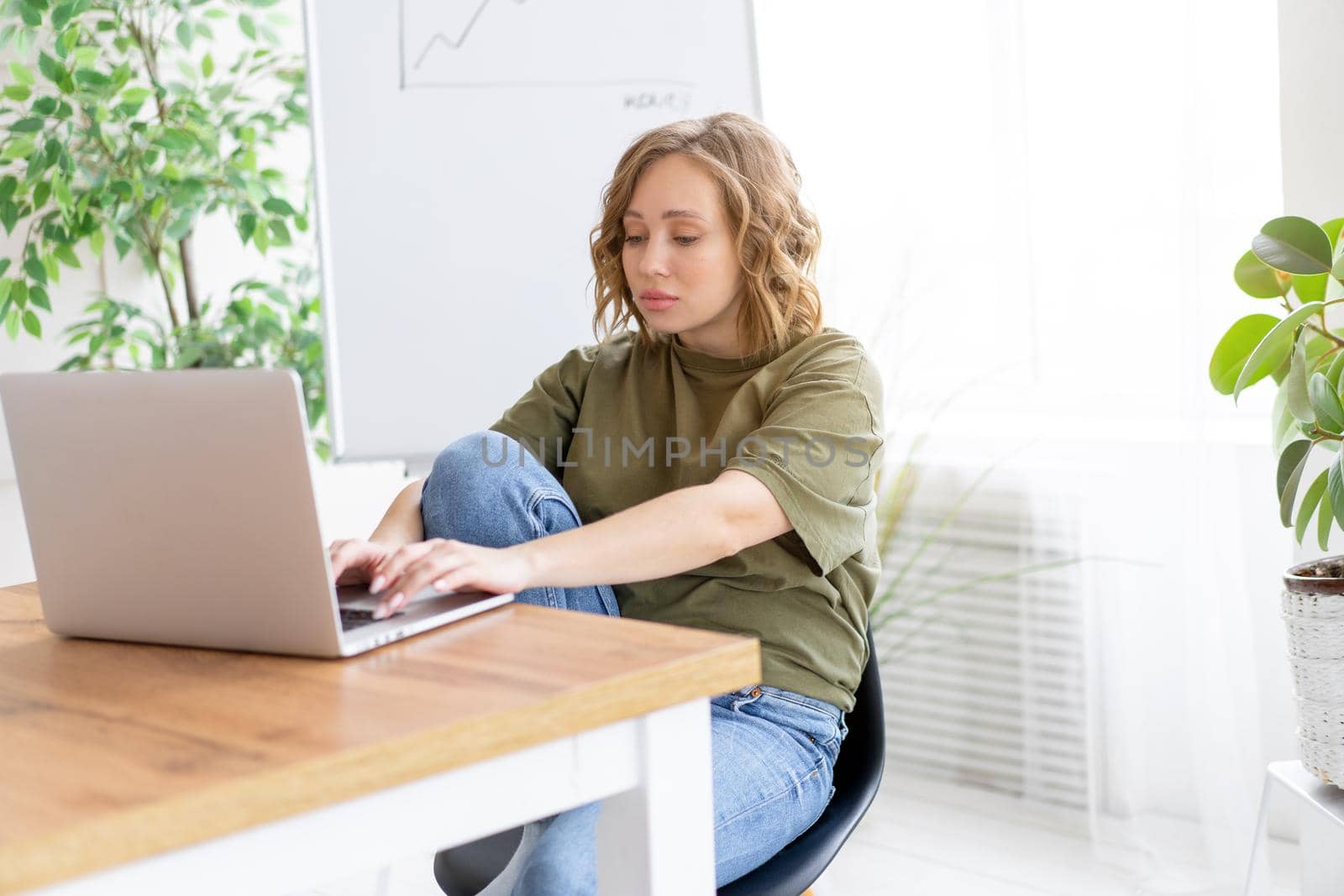 Business woman using laptop sitting desk white office interior with houseplant looking Business people Business person Online, Young and successful Dresed green shirt blue jeans barefoot relaxing