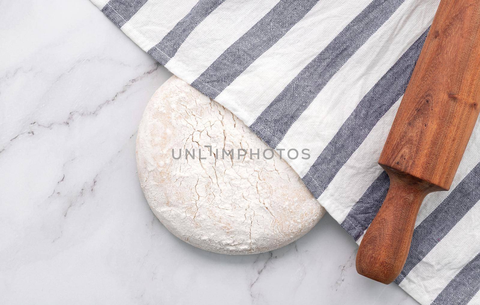 Fresh homemade yeast dough resting on marble table with rolling pin flat lay.