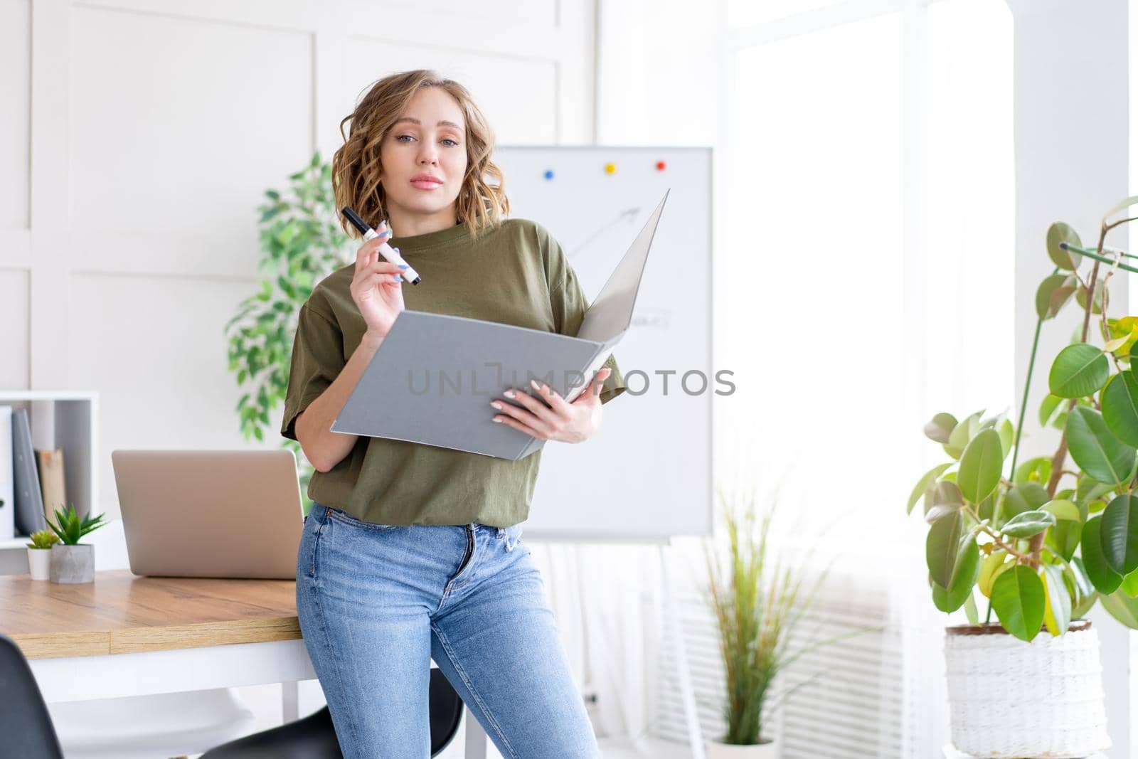 Businesswoman holding folder for paper write marker thinking dreaming standing near office table. Business person femal ypoung adult caucasian on modern white interior