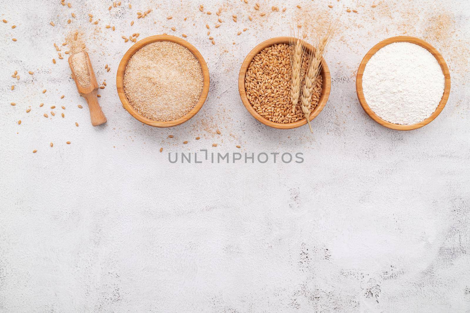 Wheat grains , brown wheat flour and white wheat flour in wooden bowl set up on white concrete background.