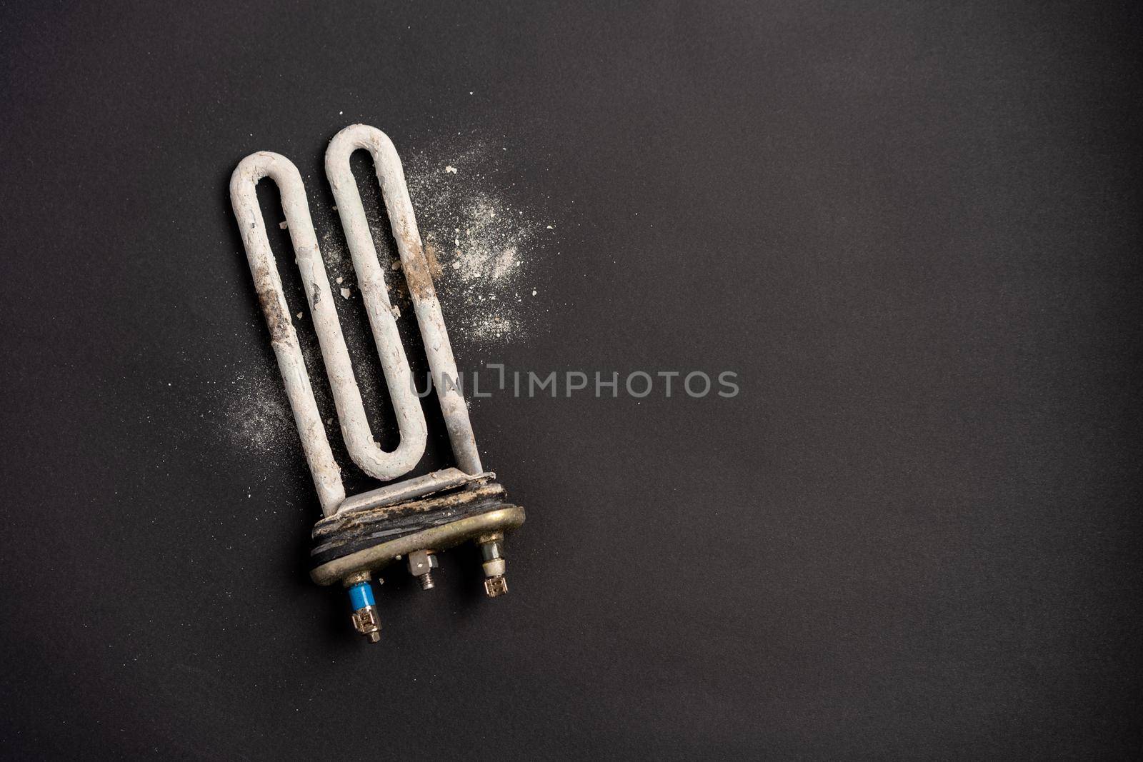 Damaged heating element of washing machine with scum and sediment on black background