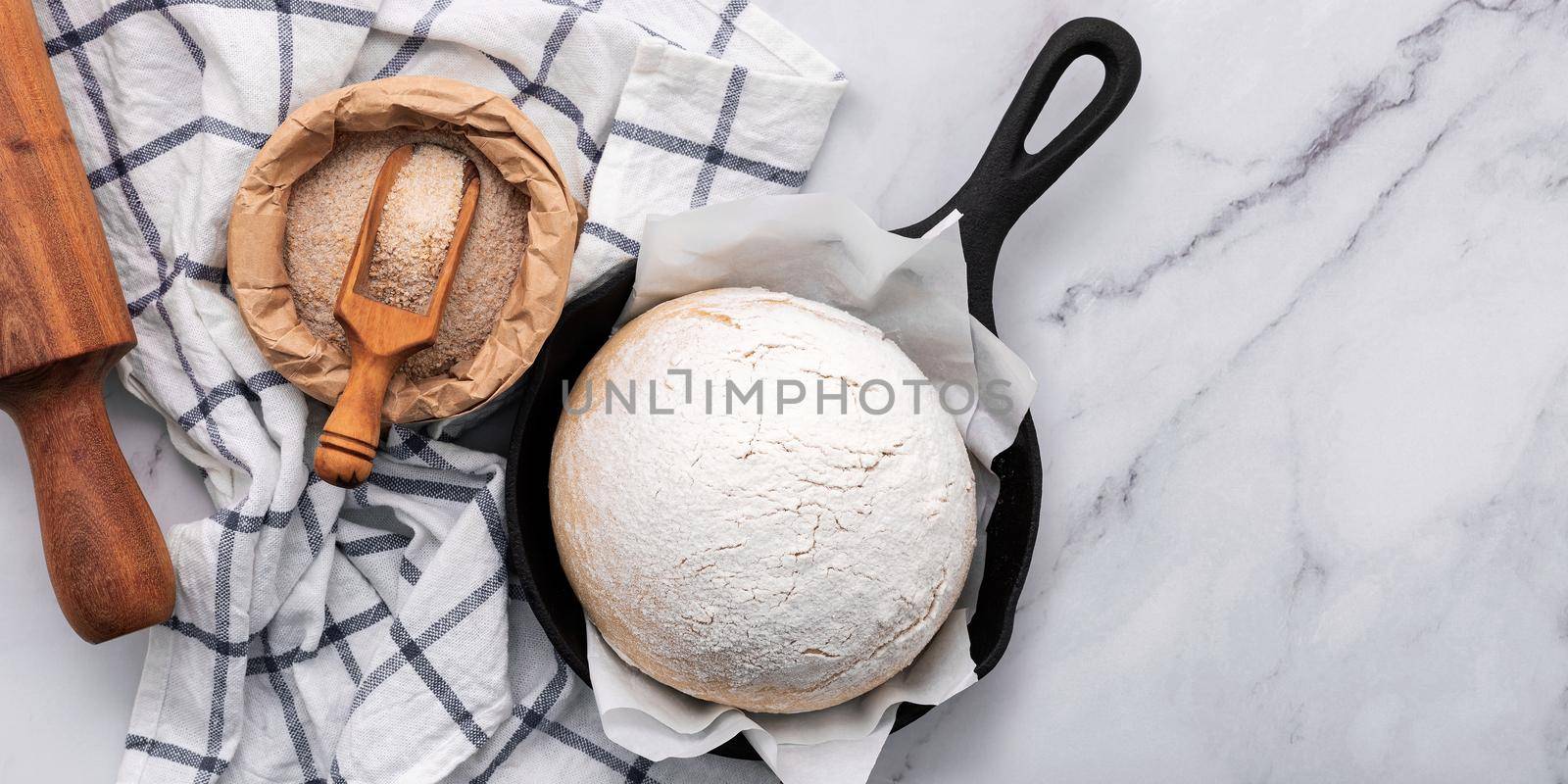 Fresh raw homemade yeast dough resting in cast iron skillet on marble table flat lay.