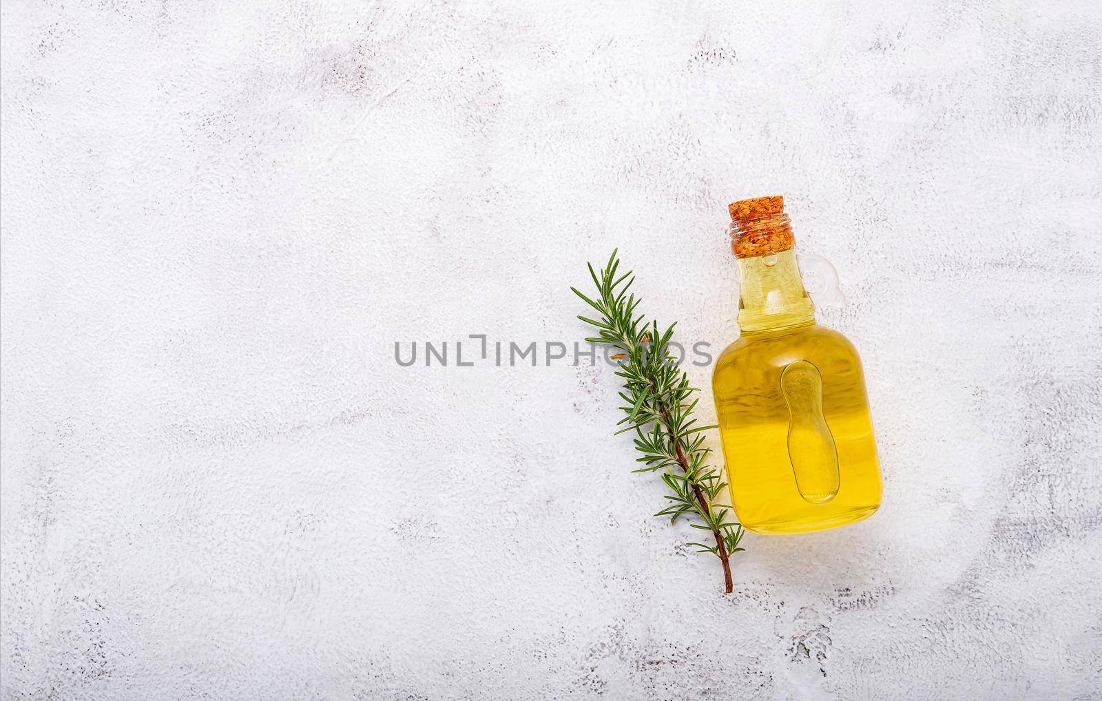 Glass bottle of olive oil and rosemary branch set up on white concrete background. by kerdkanno