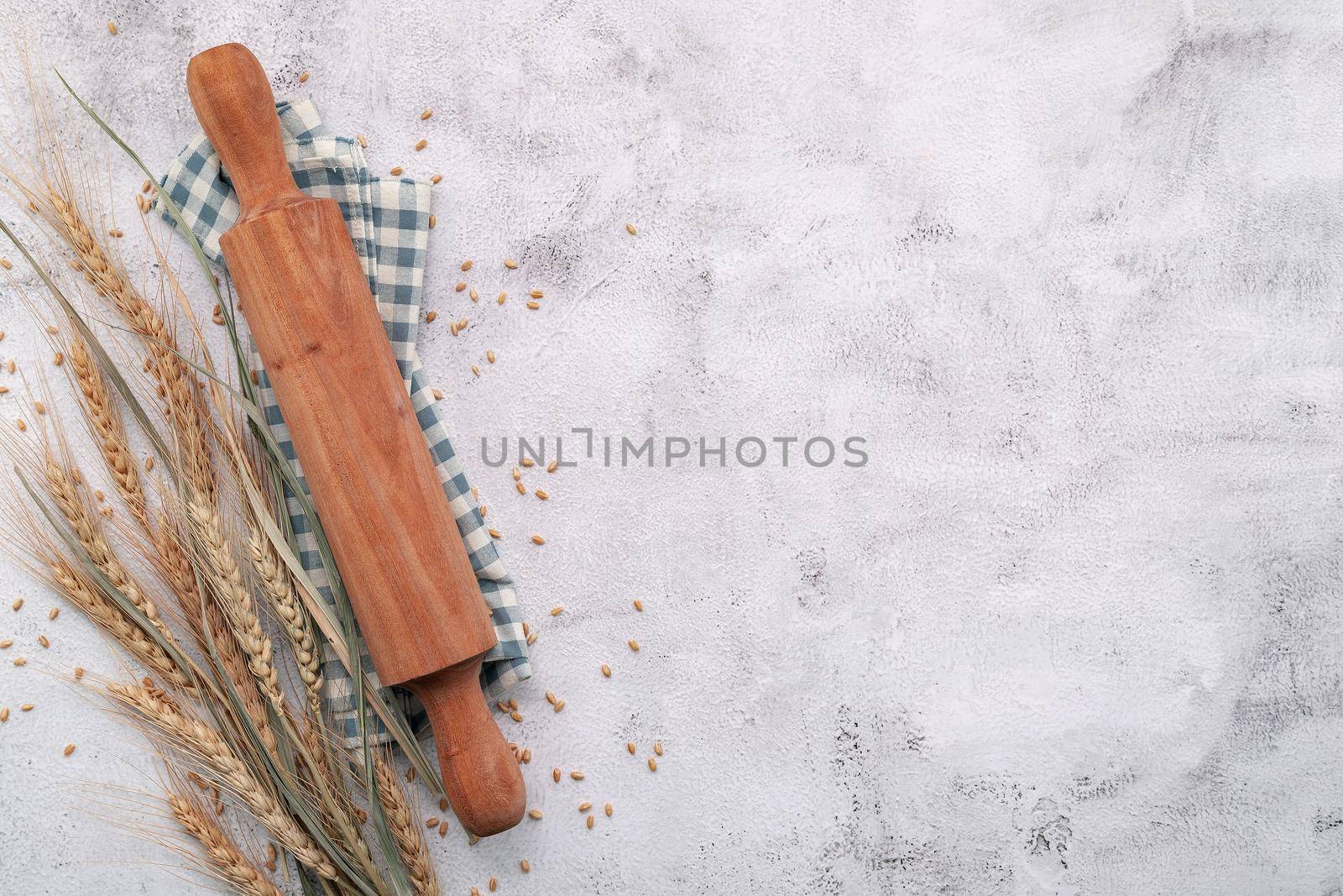 Wheat ears and wheat grains setup with rolling pin on white concrete background.