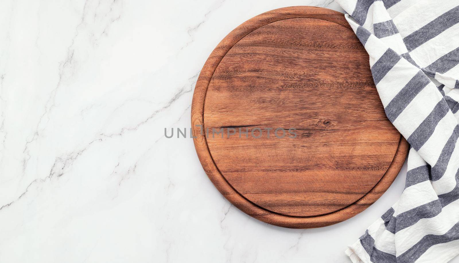 Empty wooden pizza platter with napkin set up on marble stone kitchen table. Pizza board and tablecloth on white marble background.