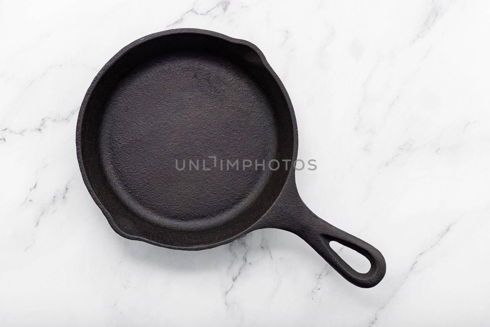 Empty old cast iron skillet set up on white marble  background with flat lay and copy space. by kerdkanno