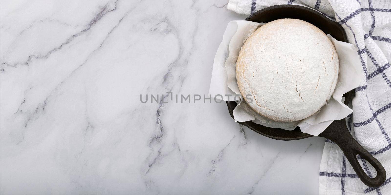 Fresh raw homemade yeast dough resting in cast iron skillet on marble table flat lay.