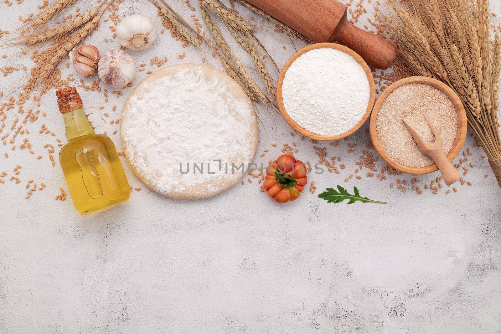 The ingredients for homemade pizza dough with wheat ears ,wheat flour and wheat grains set up on white concrete background.