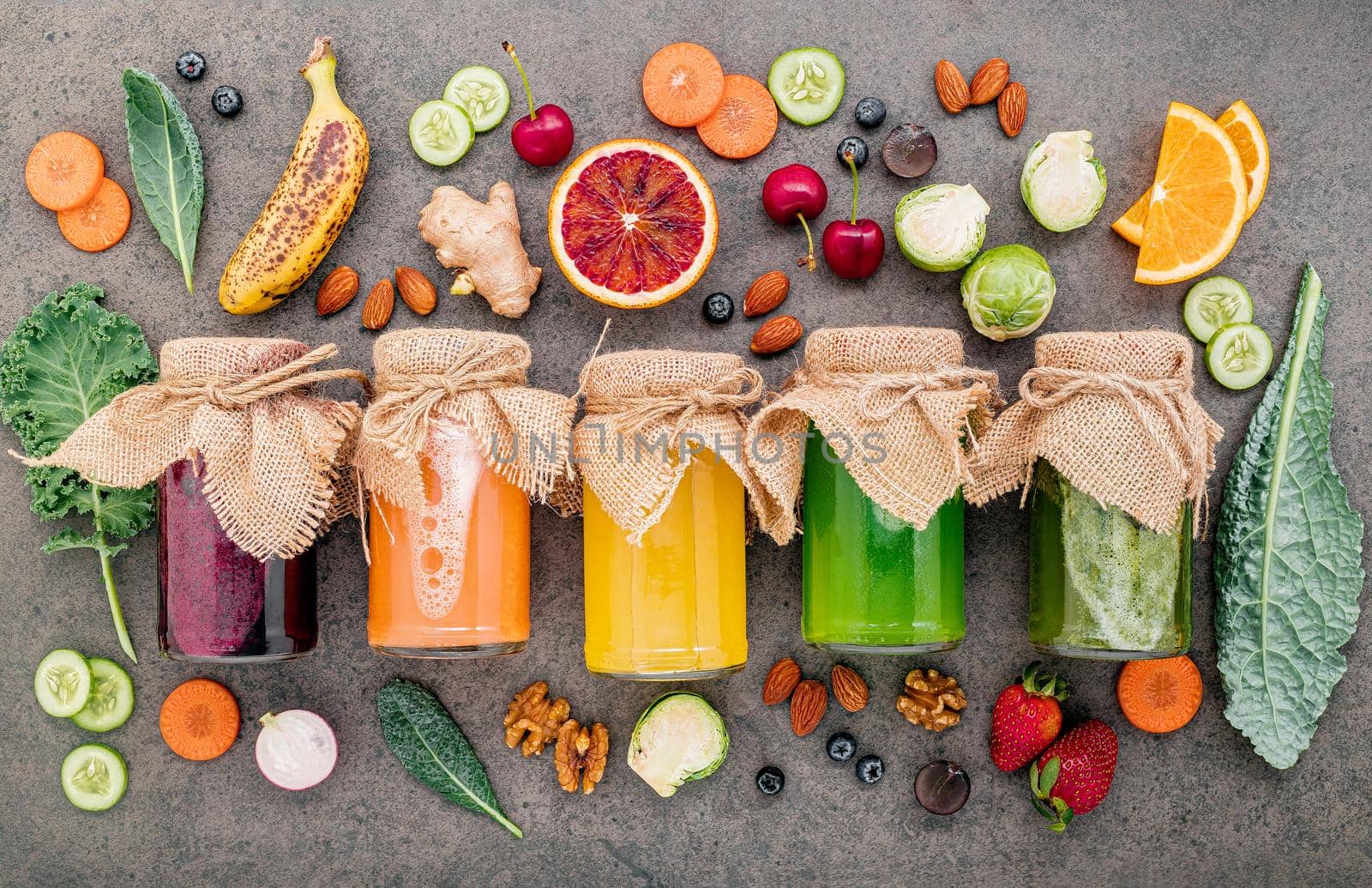 Colourful healthy smoothies and juices in bottles with fresh tropical fruit and superfoods on dark stone background with copy space.