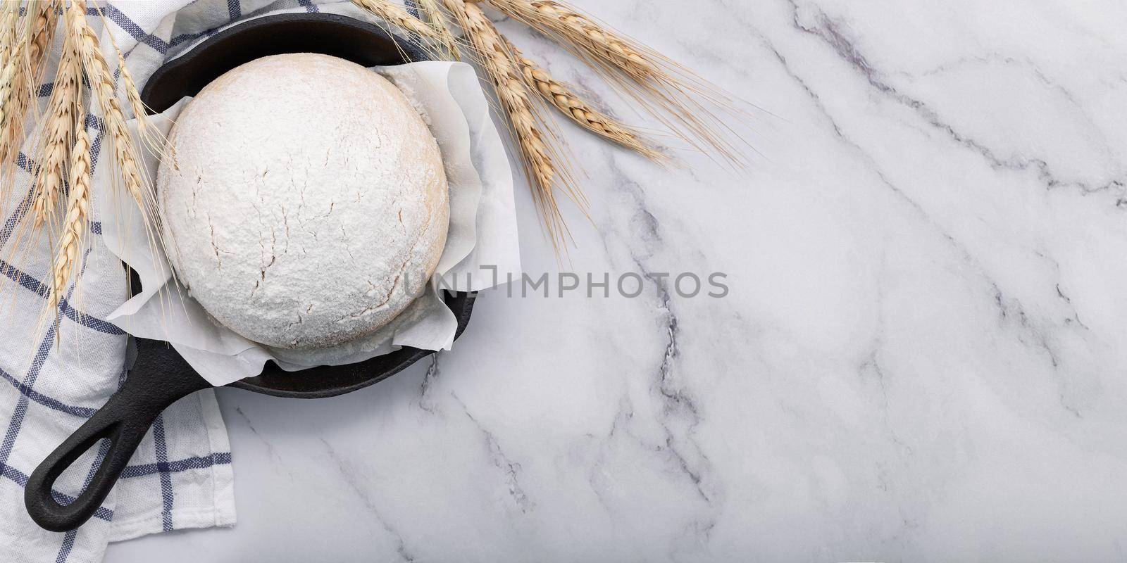 Fresh raw homemade yeast dough resting in cast iron skillet on marble table flat lay.