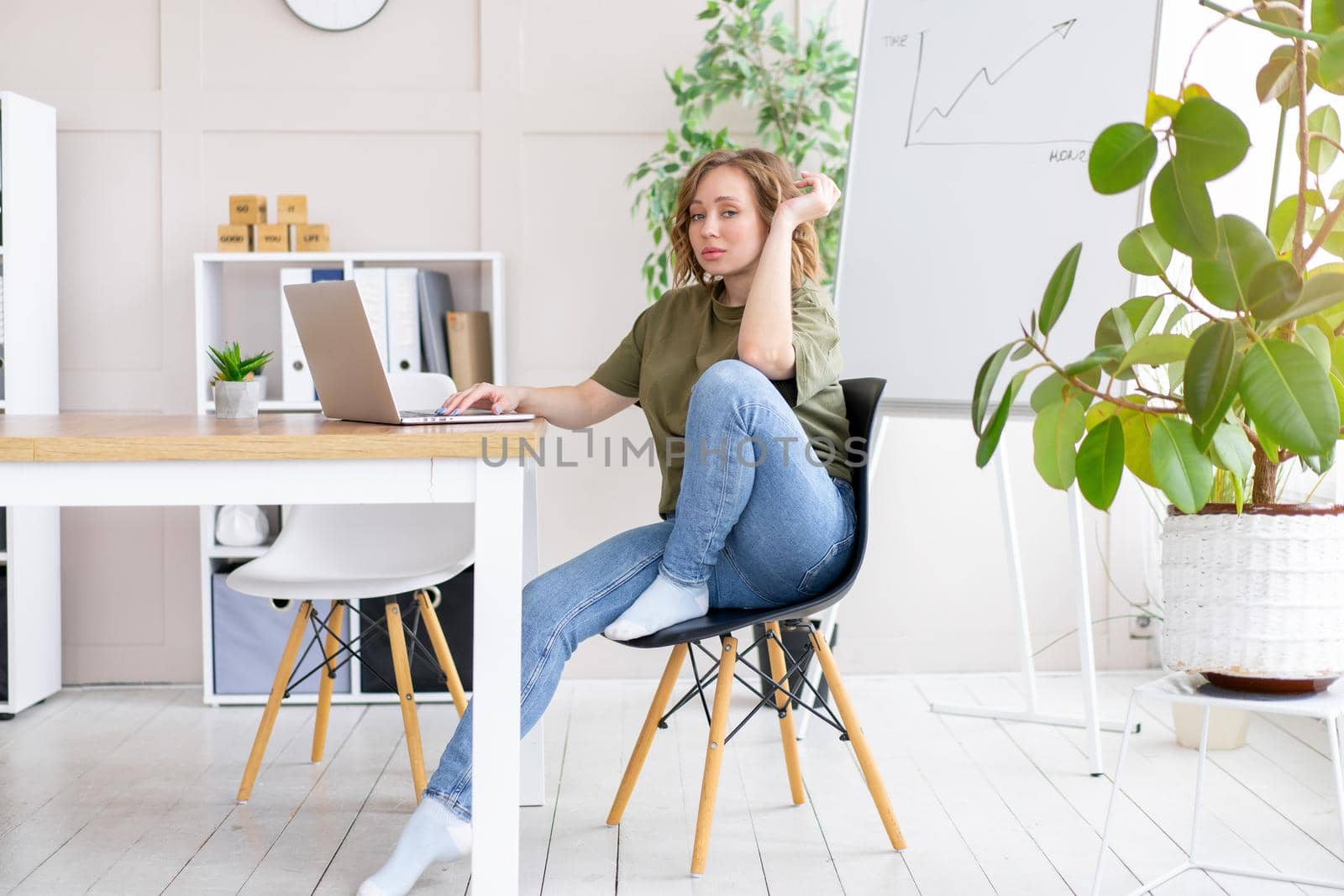 Business woman using laptop sitting desk white office interior with houseplant looking Business people Business person Online, Young and successful Dresed green shirt blue jeans barefoot relaxing