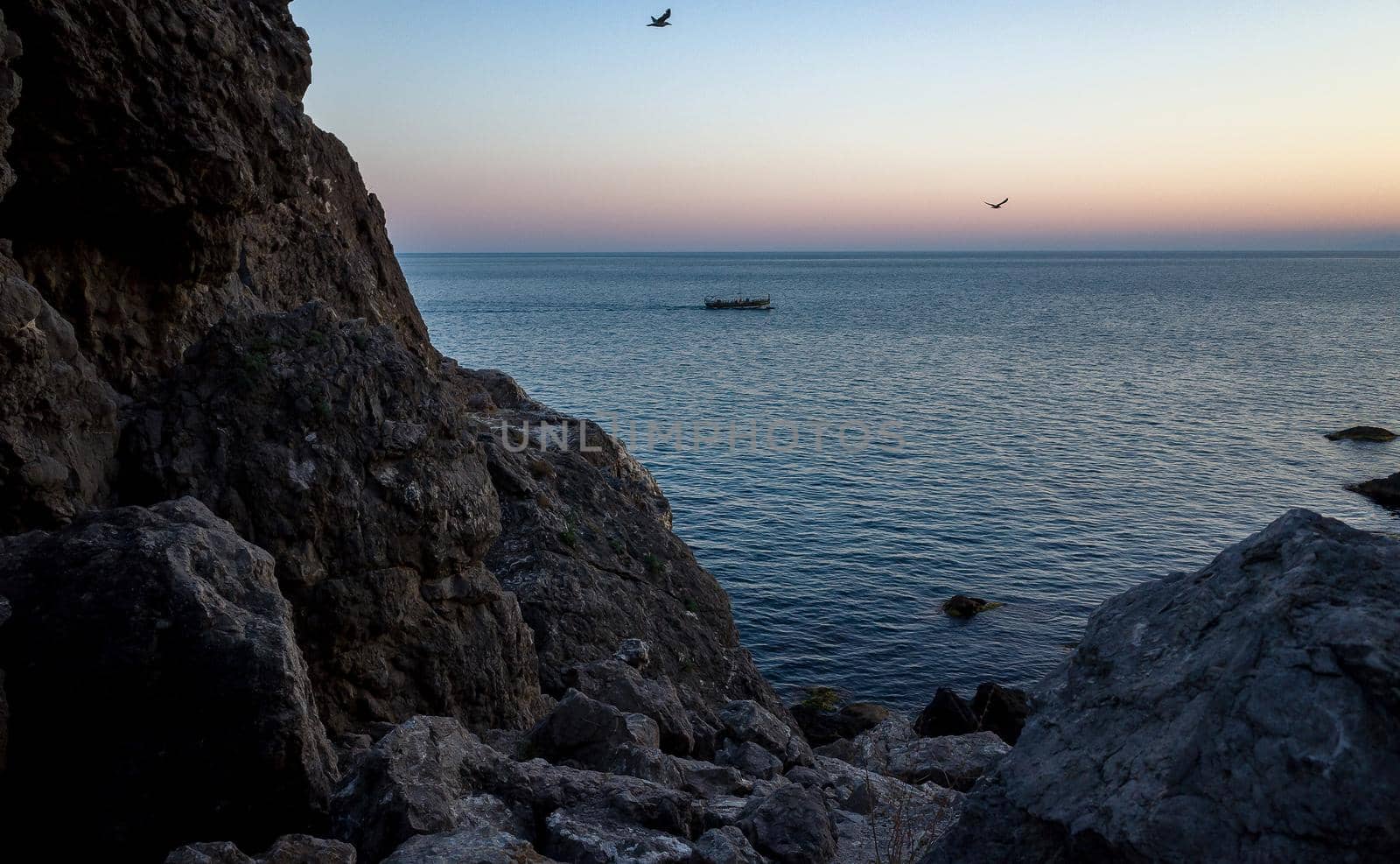 Rocky coast and a pleasure boat with tourists in the sea on a warm summer evening