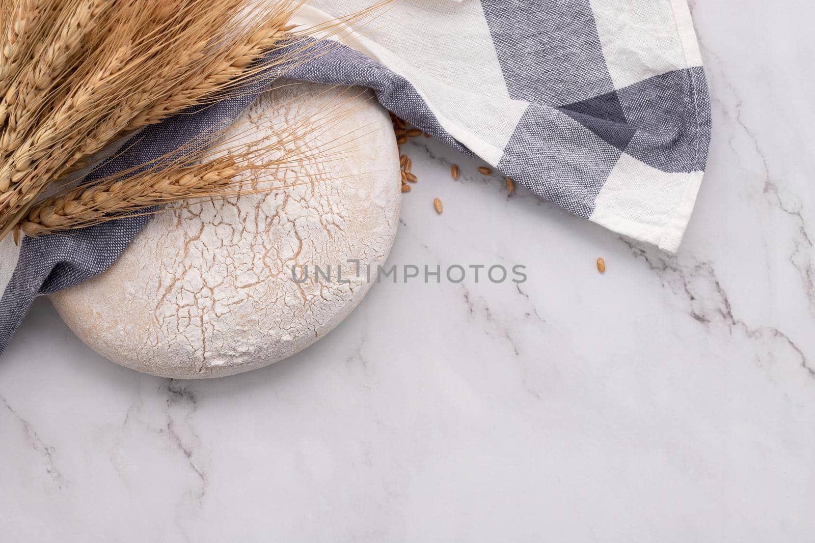 Fresh homemade yeast dough resting on marble table with ears of wheat and rolling pin. by kerdkanno