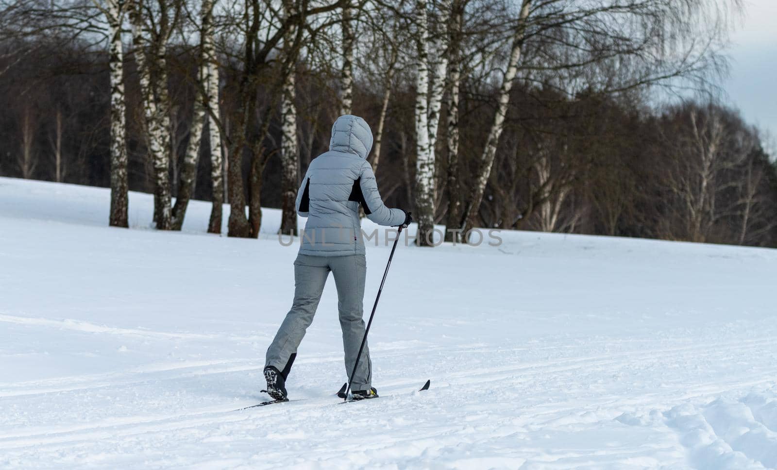 A young woman in a gray overalls is skiing through a snowy forest.