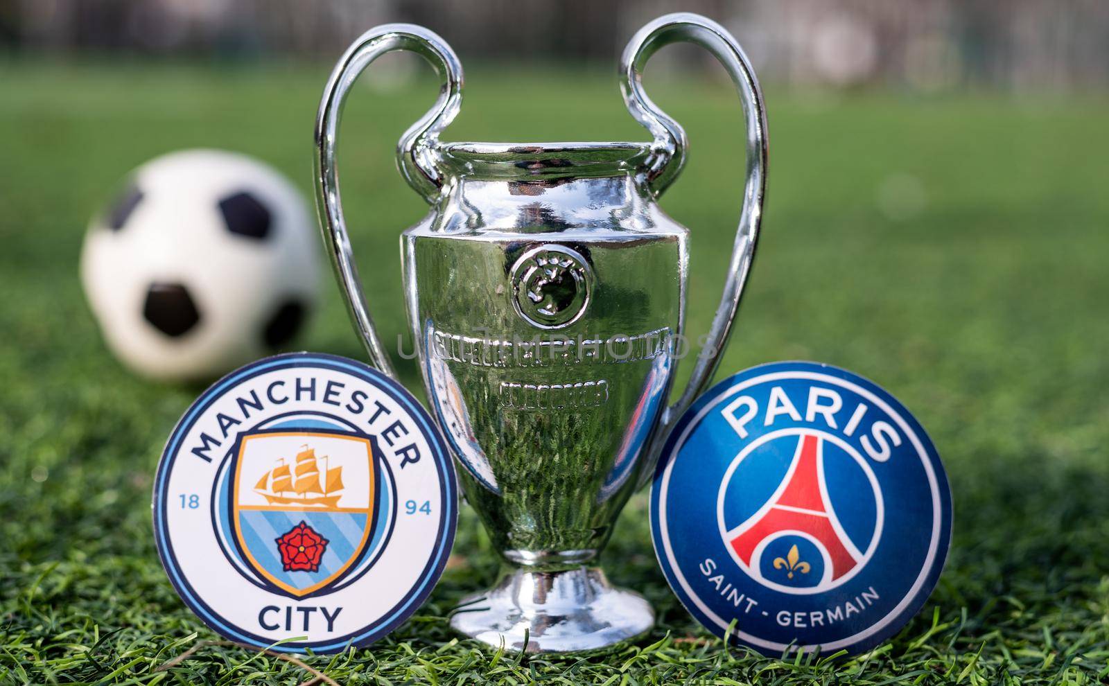 April 16, 2021 Moscow, Russia. The UEFA Champions League Cup and the emblems of the football clubs Paris Saint-Germain F. C. and Manchester City F. C. on the green grass of the lawn.