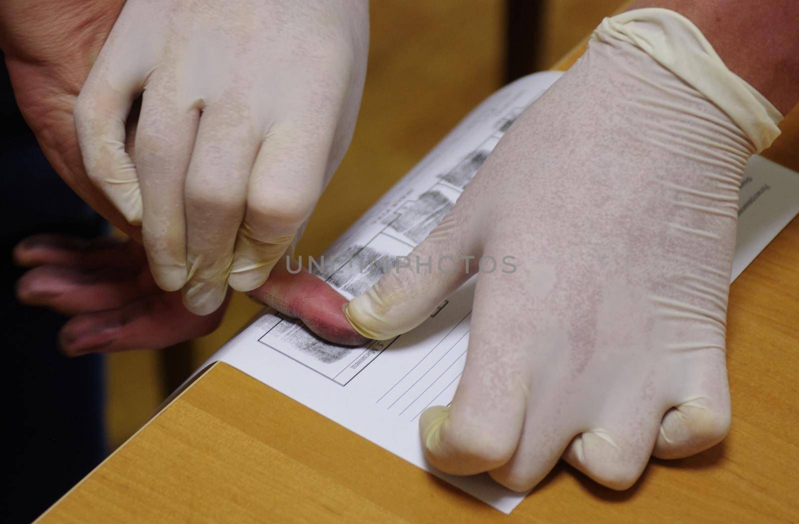 A police officer wearing rubber gloves takes a fingerprint of a suspect.