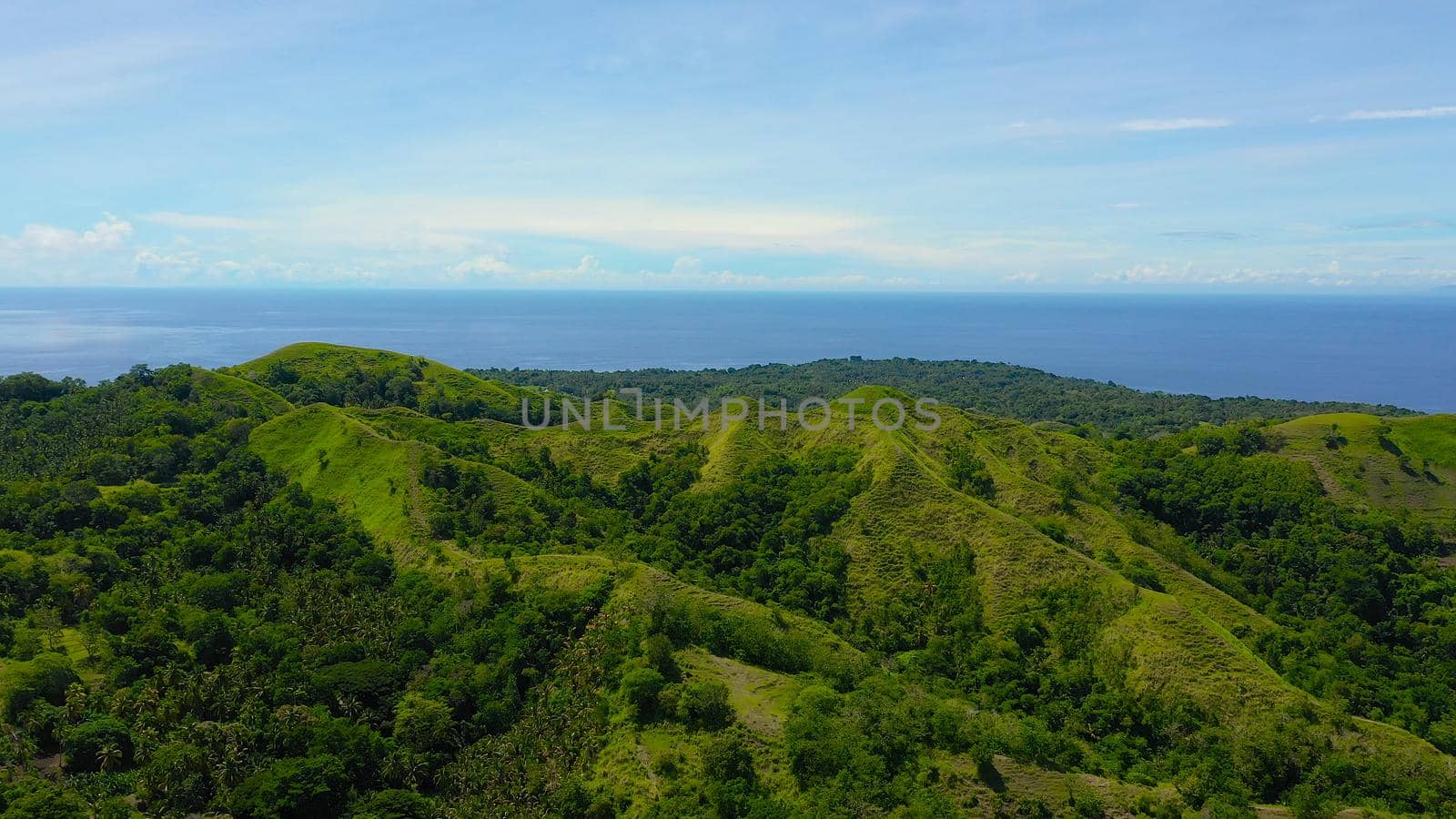 Hills and mountains covered with green grass against a background of blue sky and clouds. Bohol, Philippines. Summer landscape.