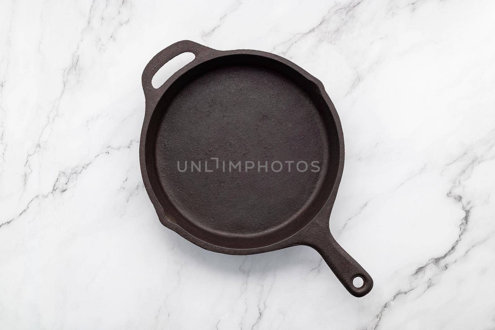 Empty old cast iron skillet set up on white marble  background with flat lay and copy space. by kerdkanno