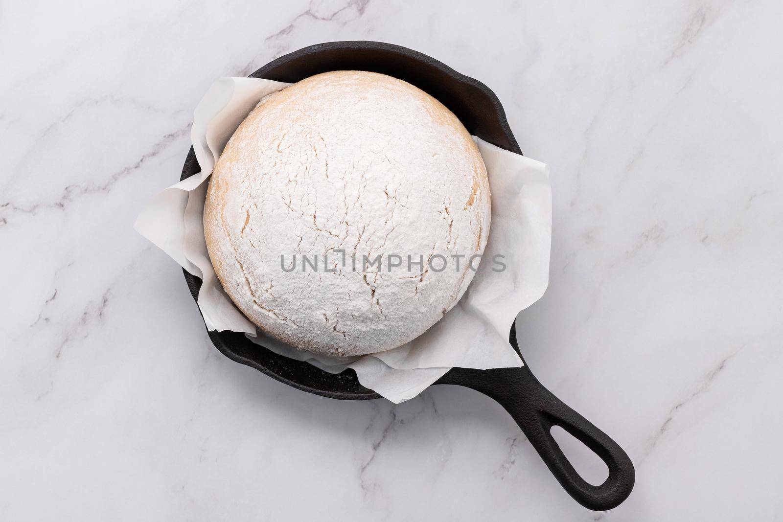 Fresh raw  homemade yeast dough resting in cast iron skillet on marble table flat lay.