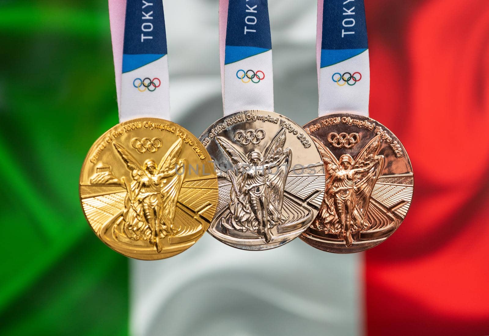 April 25, 2021 Tokyo, Japan. Gold, silver and bronze medals of the XXXII Summer Olympic Games 2020 in Tokyo on the background of the flag of Italy.