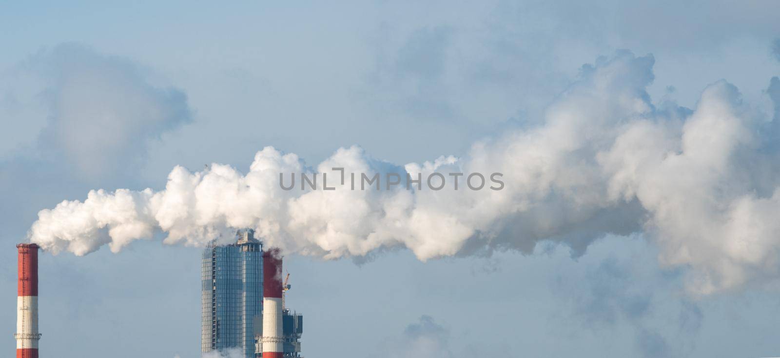 Smoke from the chimneys of a combined heat and power plant against the backdrop of a skyscraper under construction on a frosty winter day.