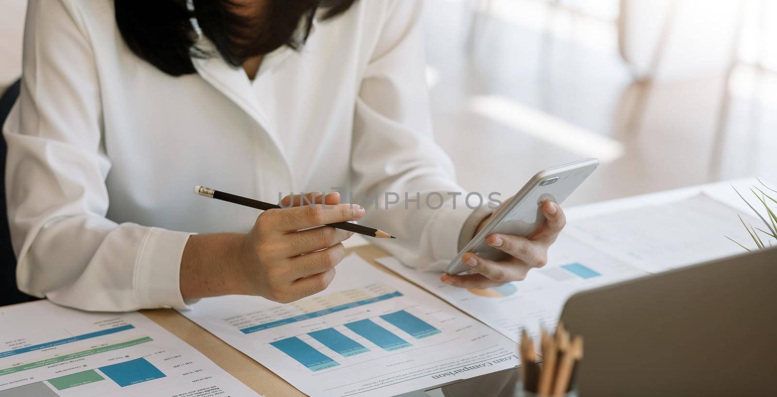 Young woman using smart phone and checking financial report and calculating expenses in the office.