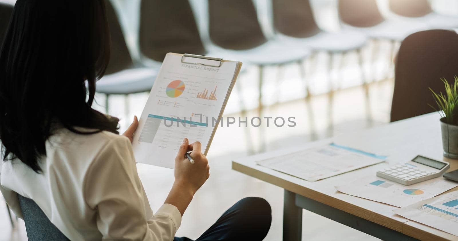 Businesswoman holding pen and pointing paper chart summary analyzing annual business report with using laptop at room office desk. Accounting Financial Concept.