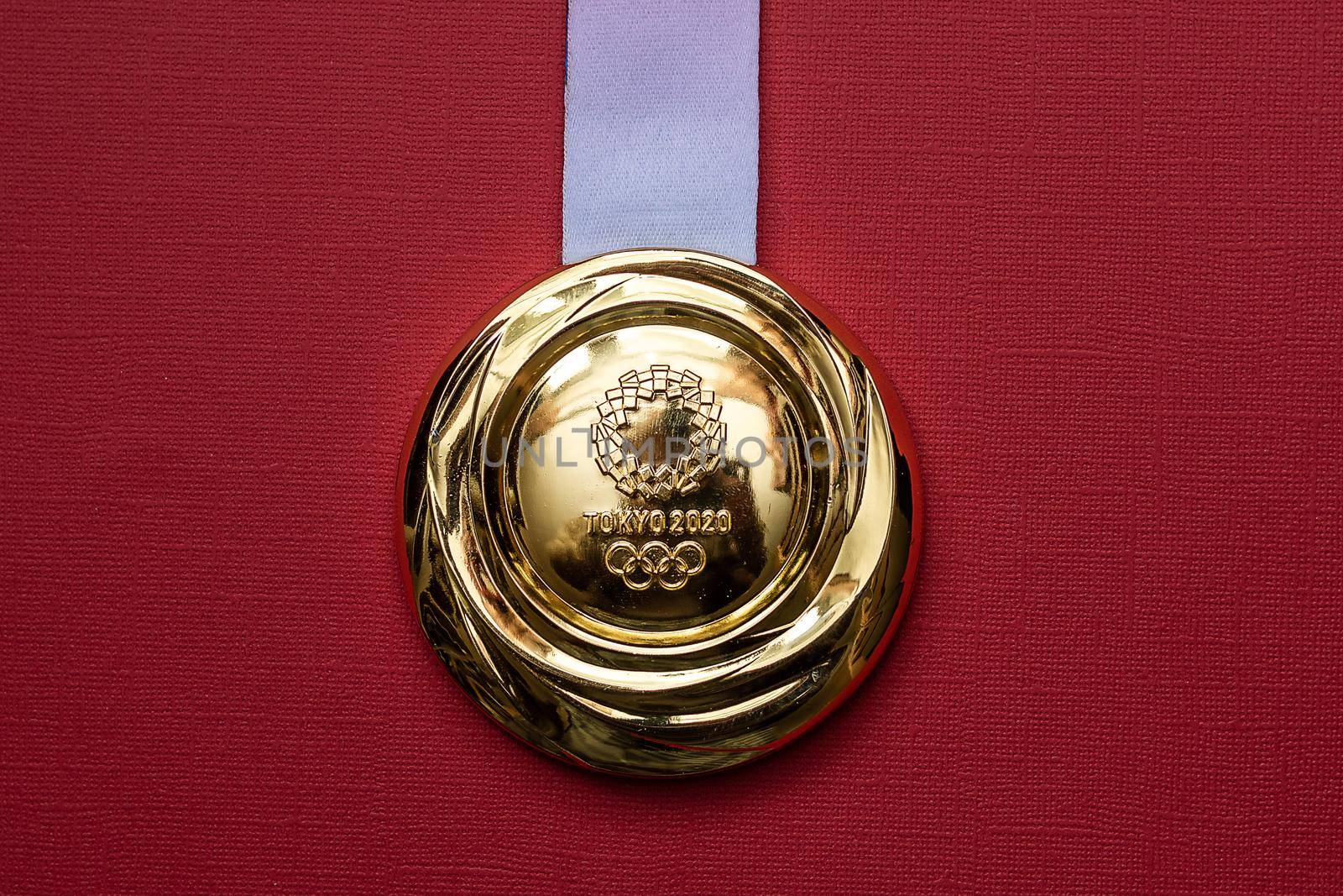 April 25, 2021 Tokyo, Japan. Gold medal of the XXXII Summer Olympic Games in Tokyo on a red background.