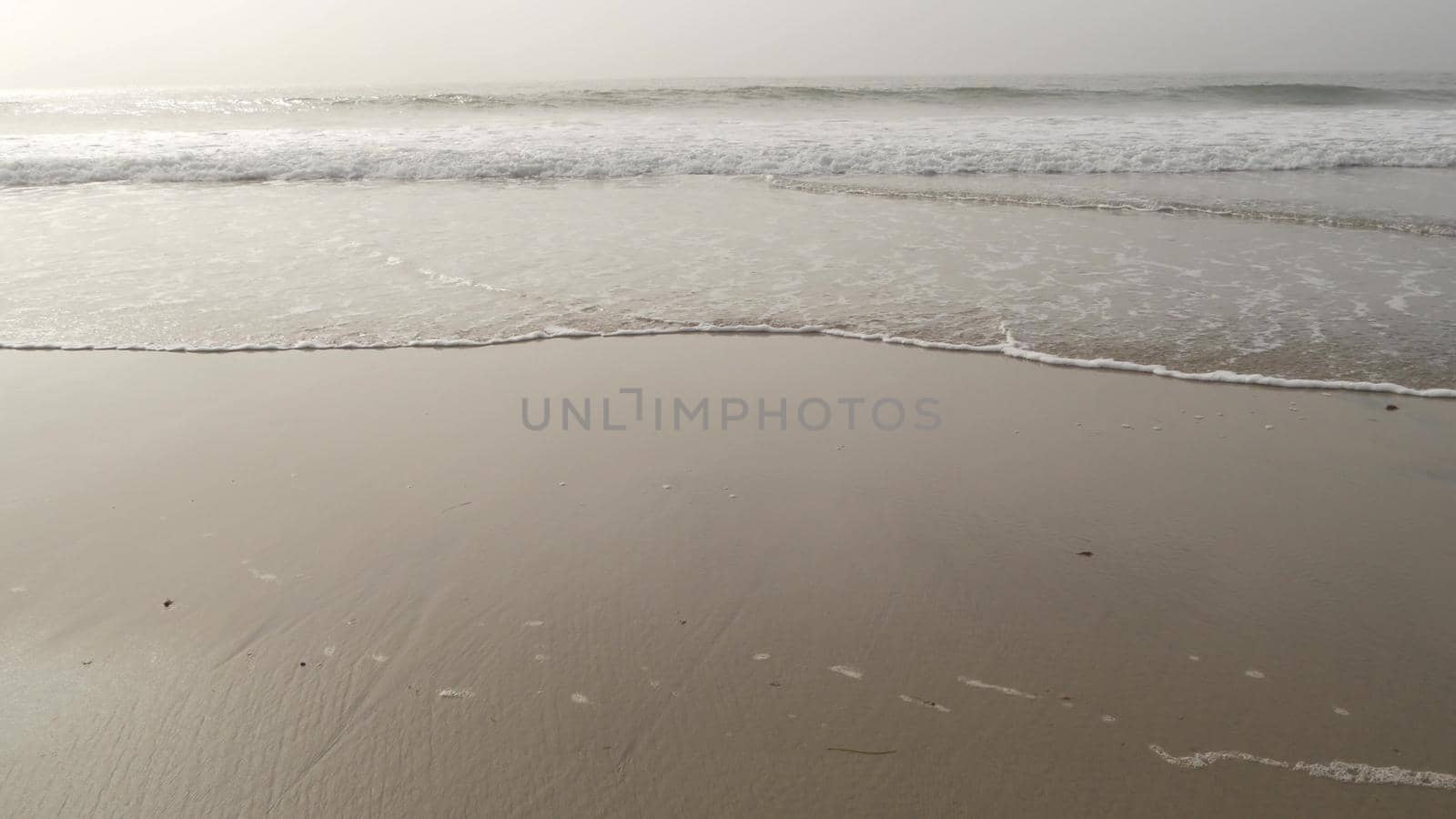 Sandy misty beach, Encinitas California USA. Pacific ocean coast, dense fog brume, empty sea shore. Coastline near Los Angeles, milky smog haze. Gloomy weather on shoreline. Grey monochrome water wave