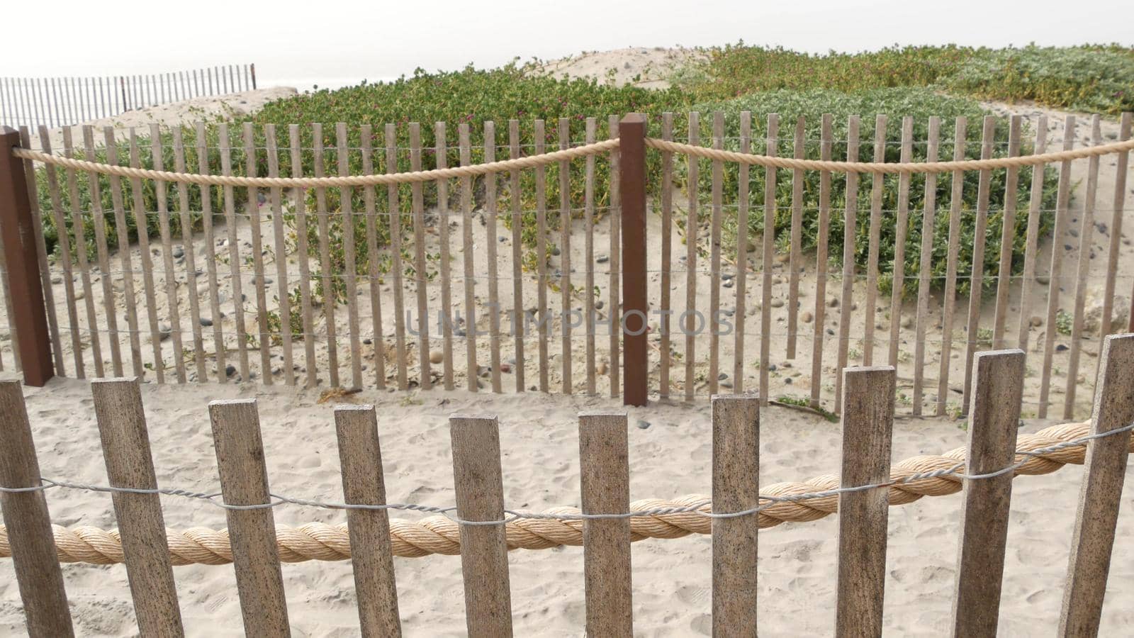 Wooden picket fence, sandy misty beach, Encinitas California USA. Pacific ocean coast, dense fog on empty sea shore. Coastline near Los Angeles, boards in milky smog haze. Gloomy weather on shoreline.