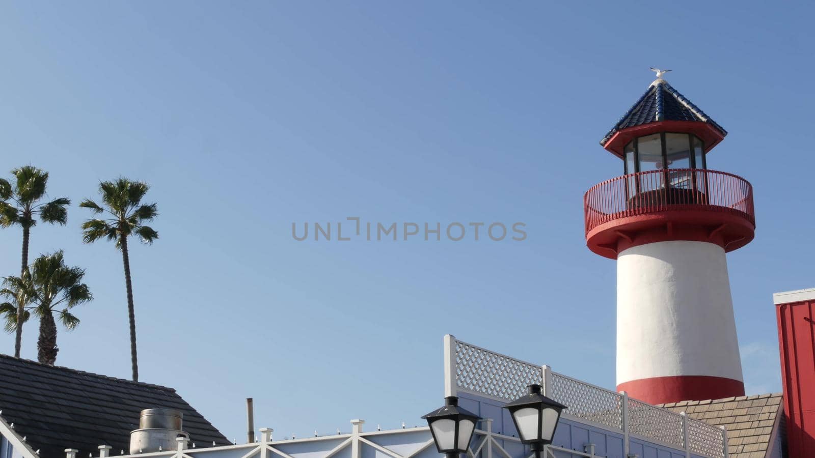 Retro lighthouse, tropical palm trees and blue sky. Red and white vintage old-fashioned beacon. Waterfront fisherman village near ocean sea harbor. Wharf or seaport, sunny summer in California USA.