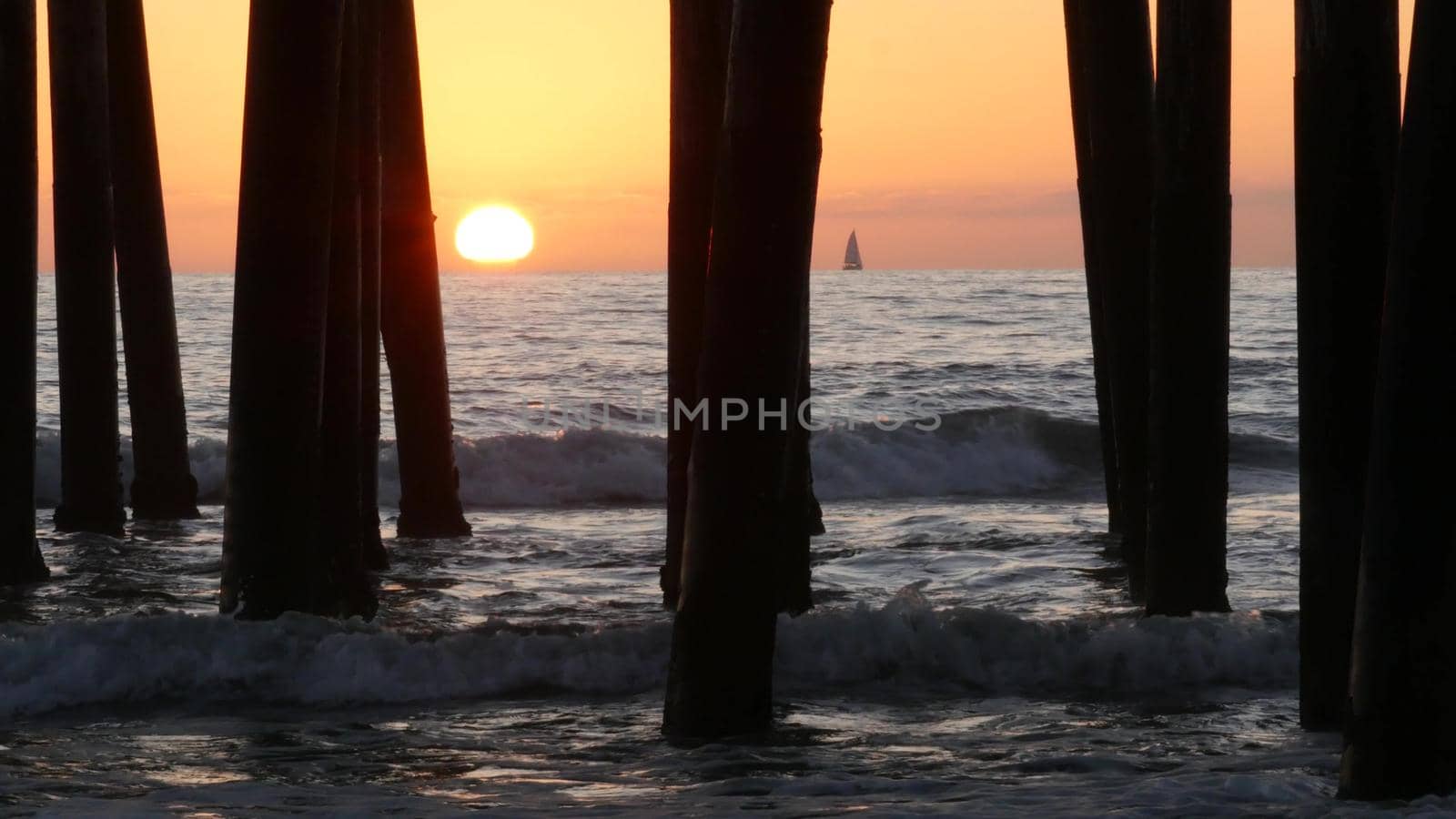 Waves splashing under pier, sunset in Oceanside, California USA. Ocean water, sun and wooden piles. by DogoraSun