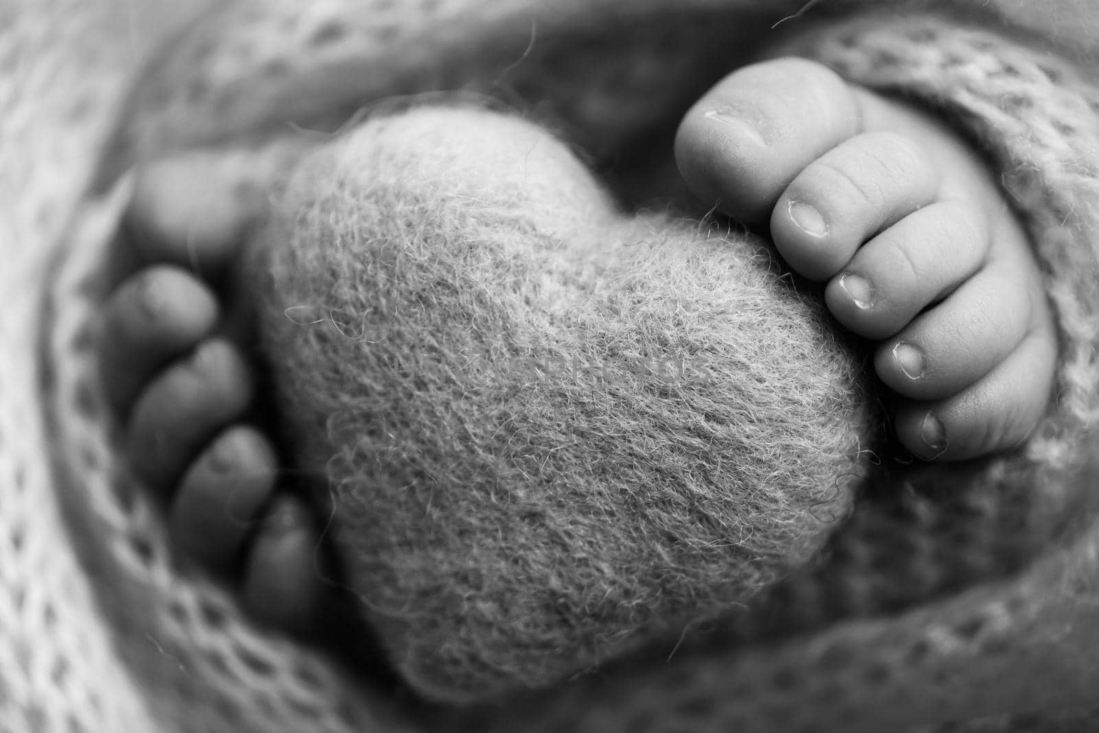 Feet of a newborn with a wooden heart, wrapped in a soft blanket. by Vad-Len