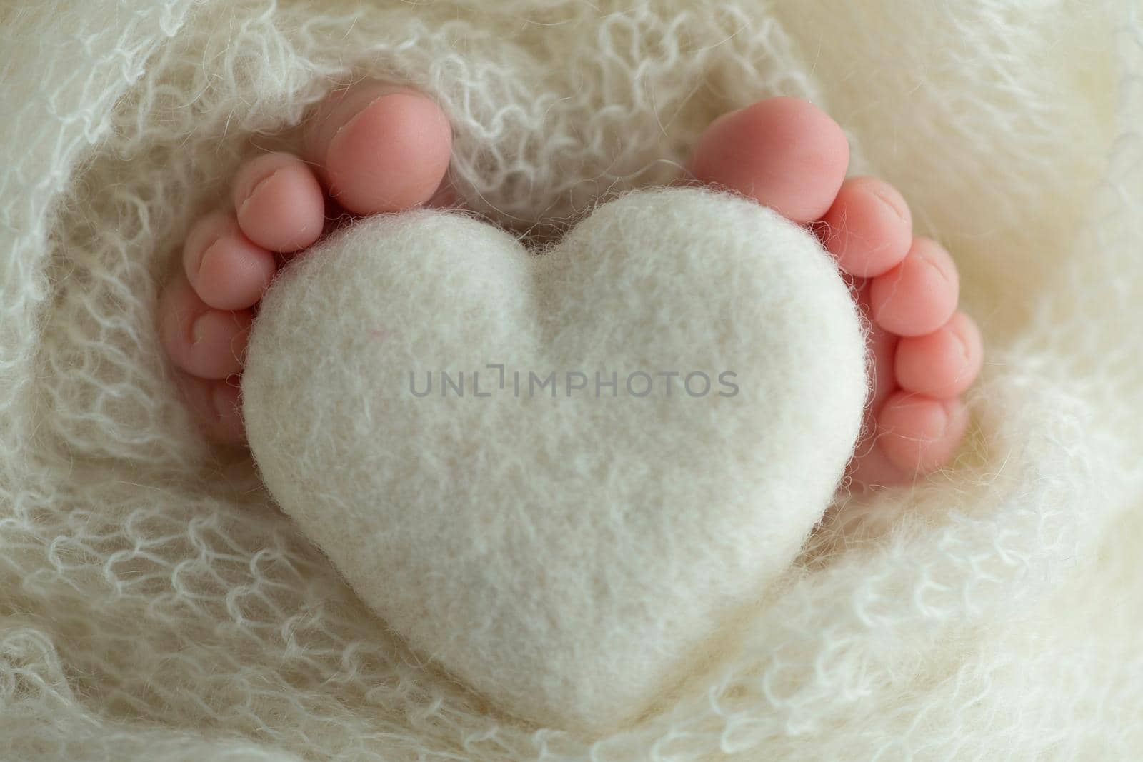 Two cute tiny baby feet wrapped in white knitted blanket. And a knitted heart made of woolen threads. by Vad-Len