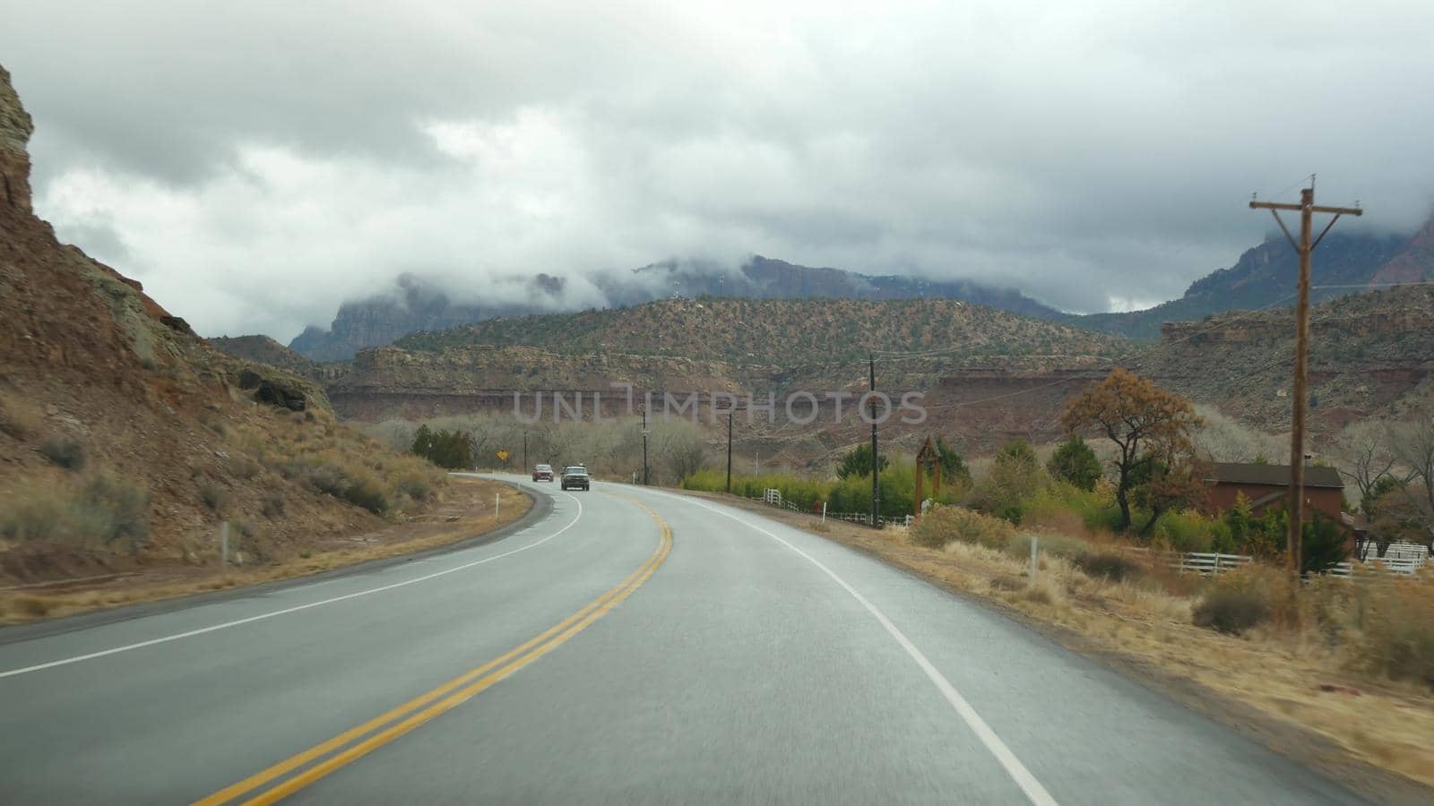 Road trip, driving auto in Zion Canyon, Utah, USA. Hitchhiking traveling in America, autumn journey. Red alien steep cliffs, rain and bare trees. Foggy weather and calm fall atmosphere. View from car.