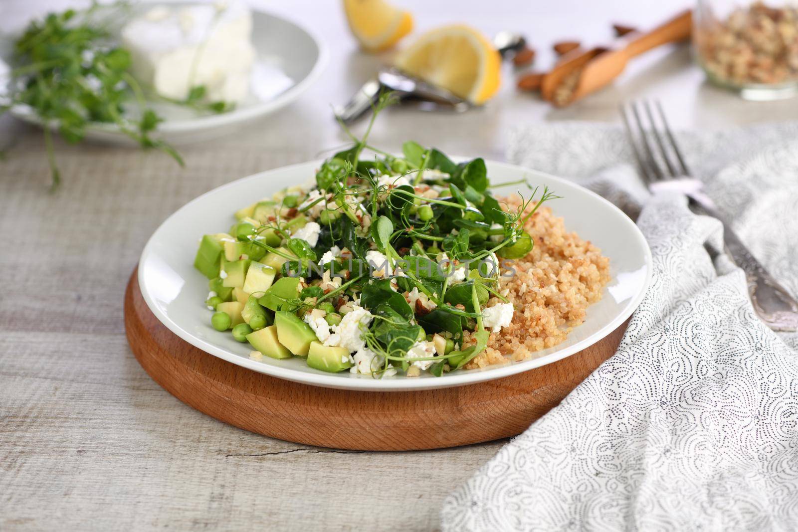 Gluten-free green vegetarian salad made of microgreen sprouts peas, avocado, quinoa, spinach, seasoned  crushed almonds with slices of feta cheese