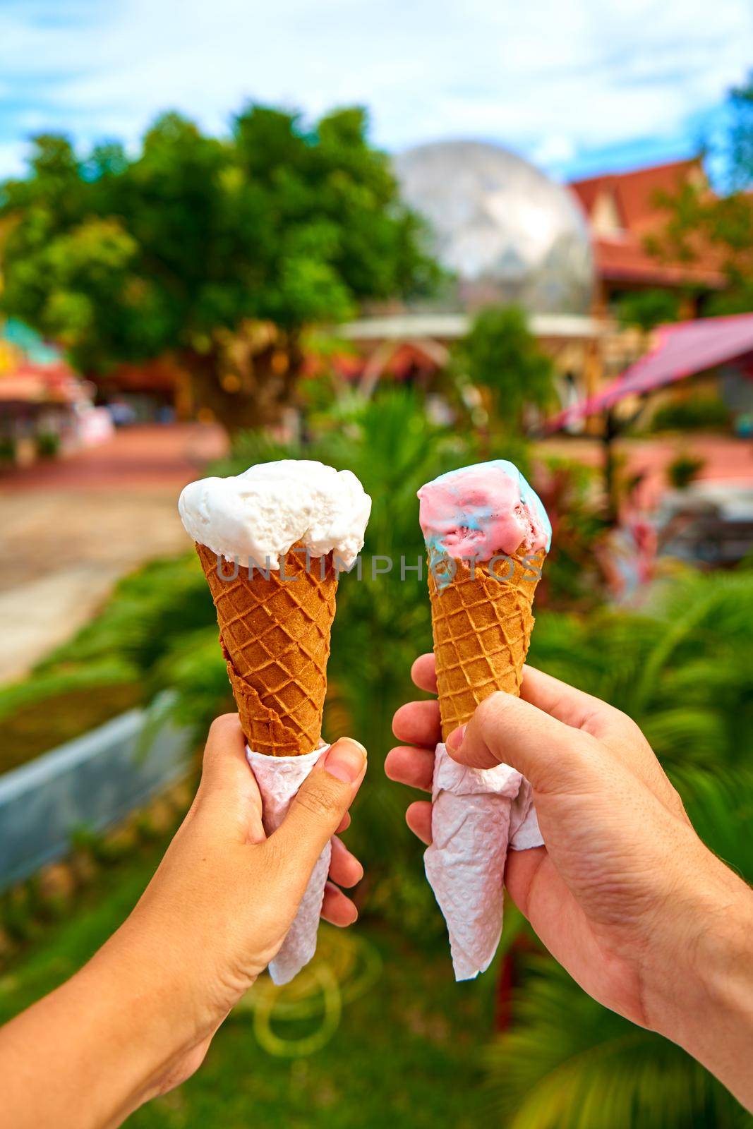 A couple takes pictures of ice cream cones in their hands.