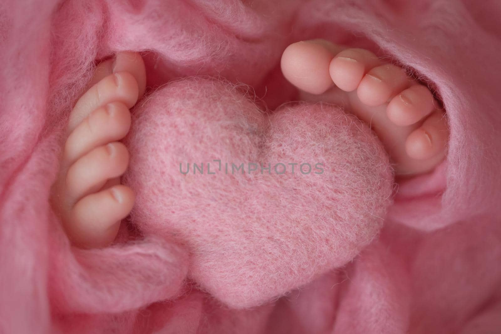 Two cute tiny baby feet wrapped in pink knitted blanket. And a knitted heart made of woolen threads. by Vad-Len