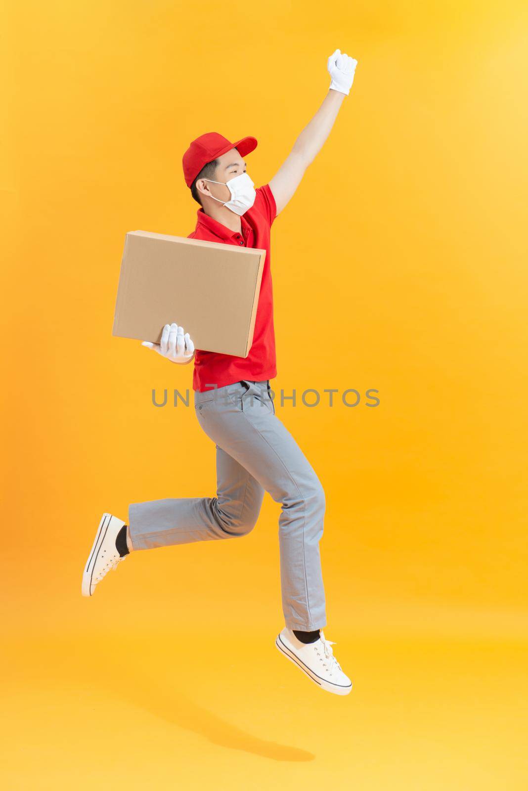 delivery man with face mask and gloves holding a cardboard box and jumping by makidotvn