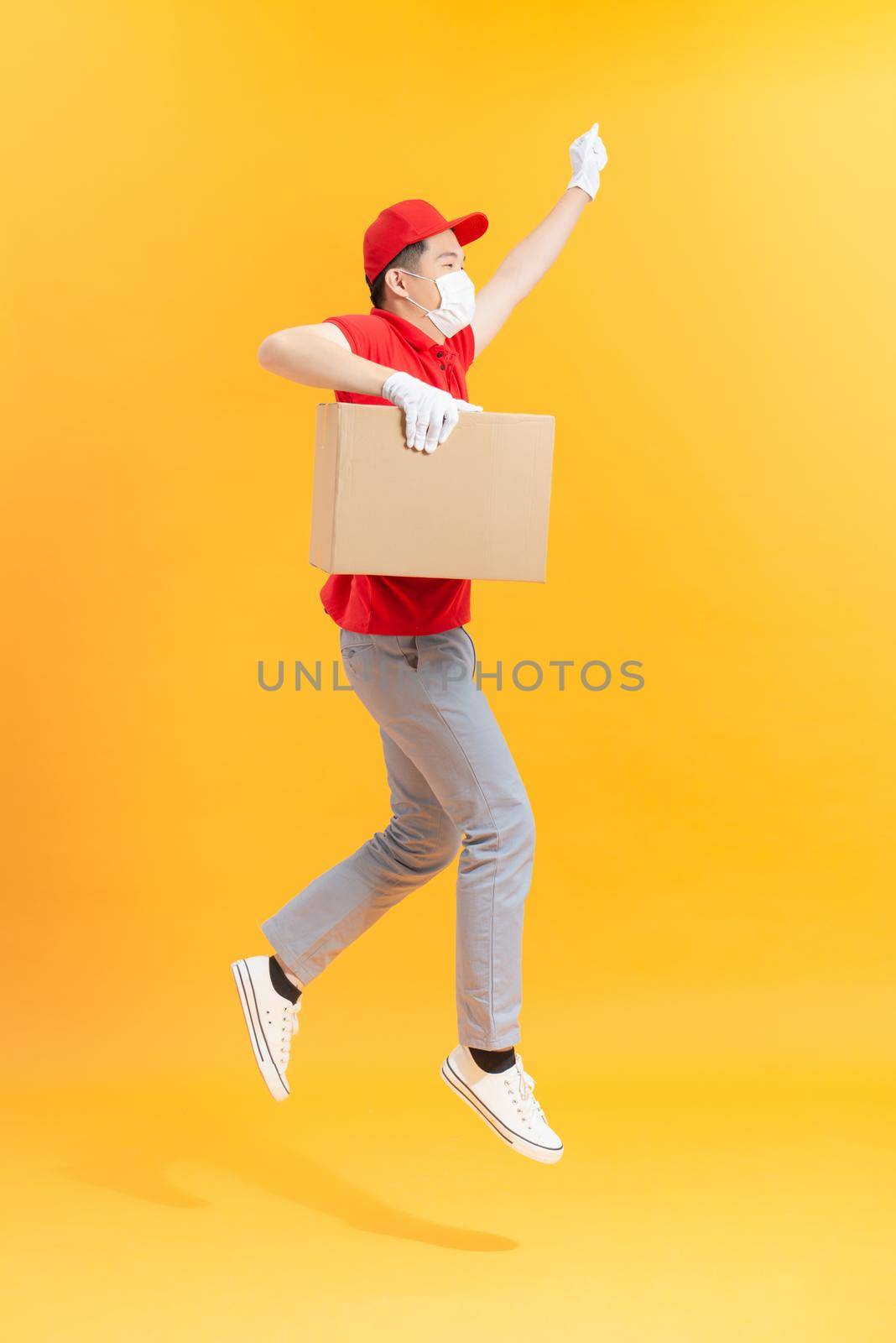 Running male courier in medical mask and protective gloves with boxes