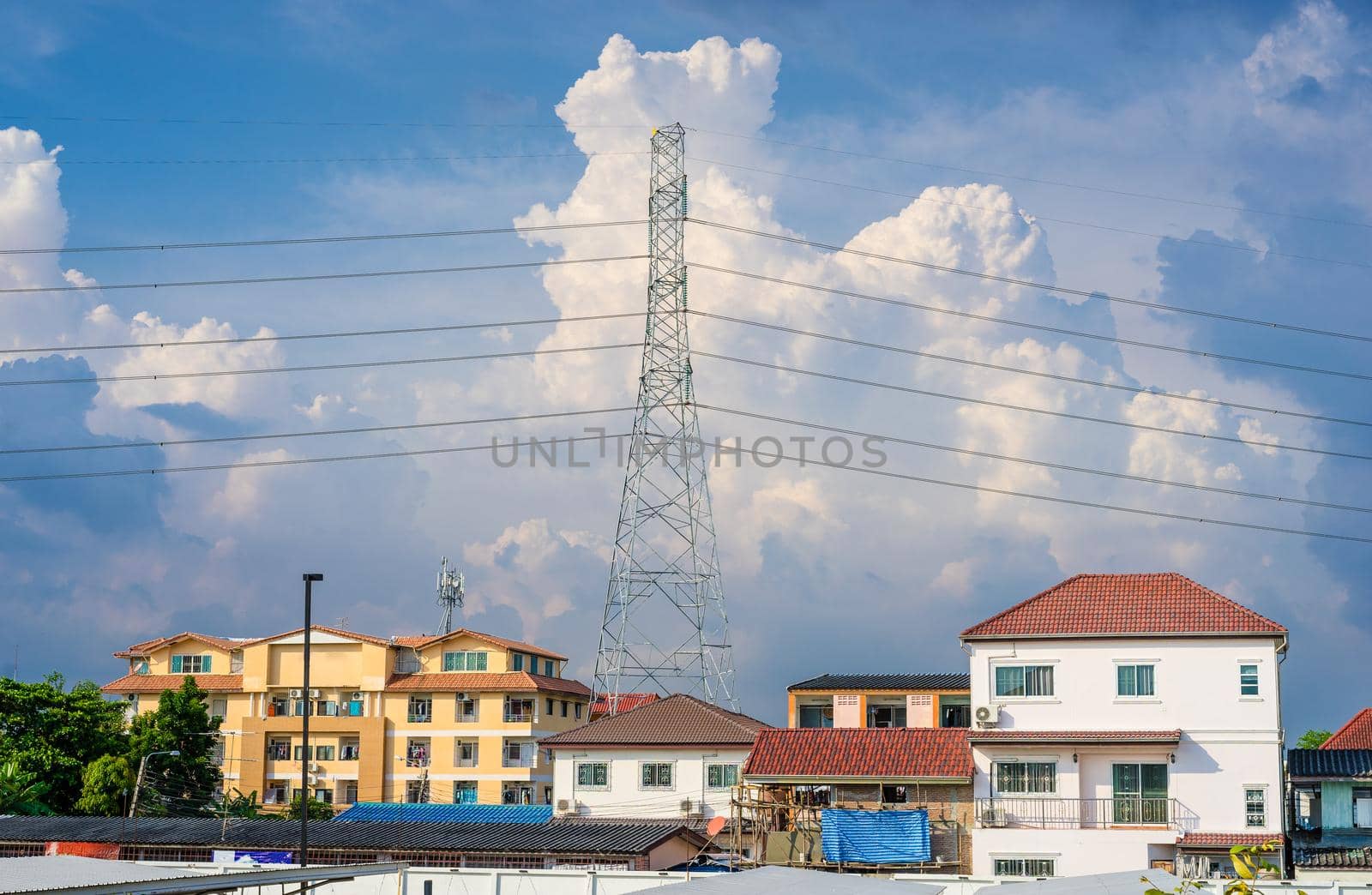 Background of electricity pole system with home in city with cloudy sky by domonite