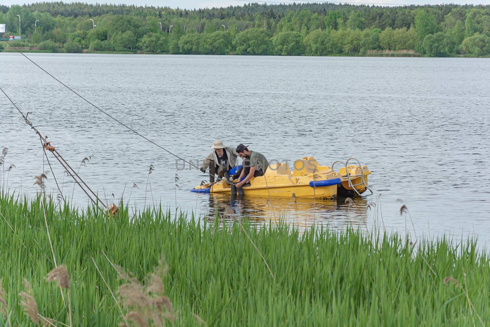 BELARUS, MINSK - MAY 28, 2021: Men on a catamaran repair an anchorage rope. Stock photography.