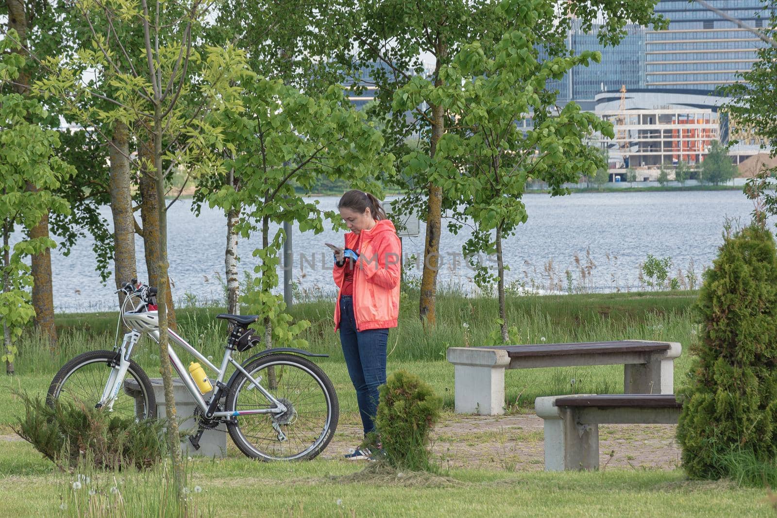 Belarus, Minsk - May 28, 2021: A woman with a bicycle is resting in the park and looks into a smartphone. Stock photography.