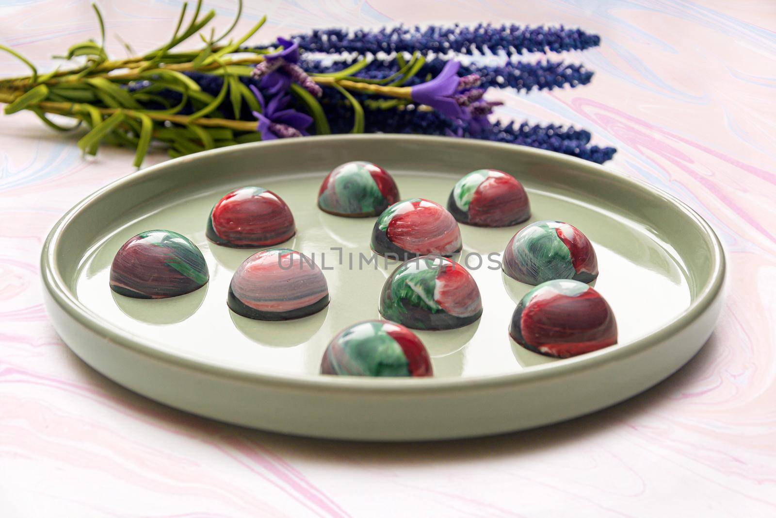 Collectible handmade tempered chocolate candies with a glossy painted body on a round plate with a blurred background and bokeh elements. Stock photography.
